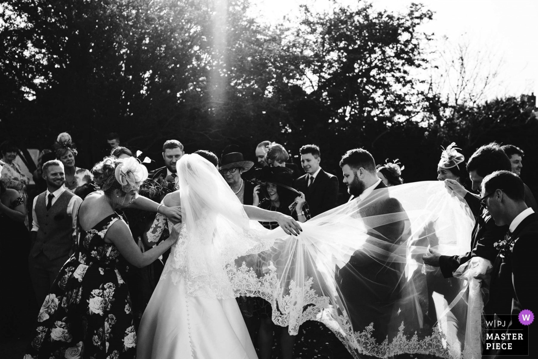 The bride is backlit by sunlight as her veil is adjusted by friends and family at Southwold church. 