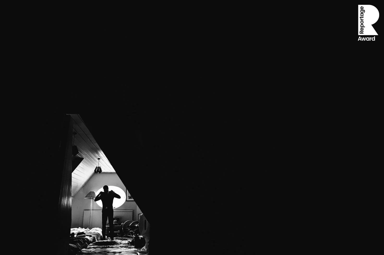 A groom silhouetted against a window as he puts on his jacket before a wedding at Voewood, North Norfolk.