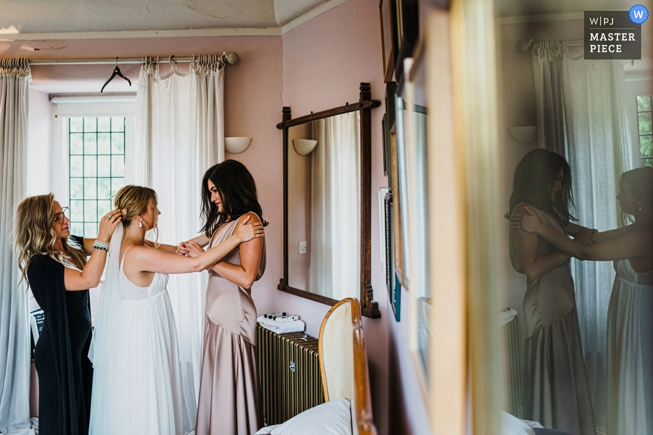a bride and bridesmaid embrace during the last moments of the bridal prep as the hair and makeup artist puts the finishing touches to the brides hair in the bridal suite at Voewood. 