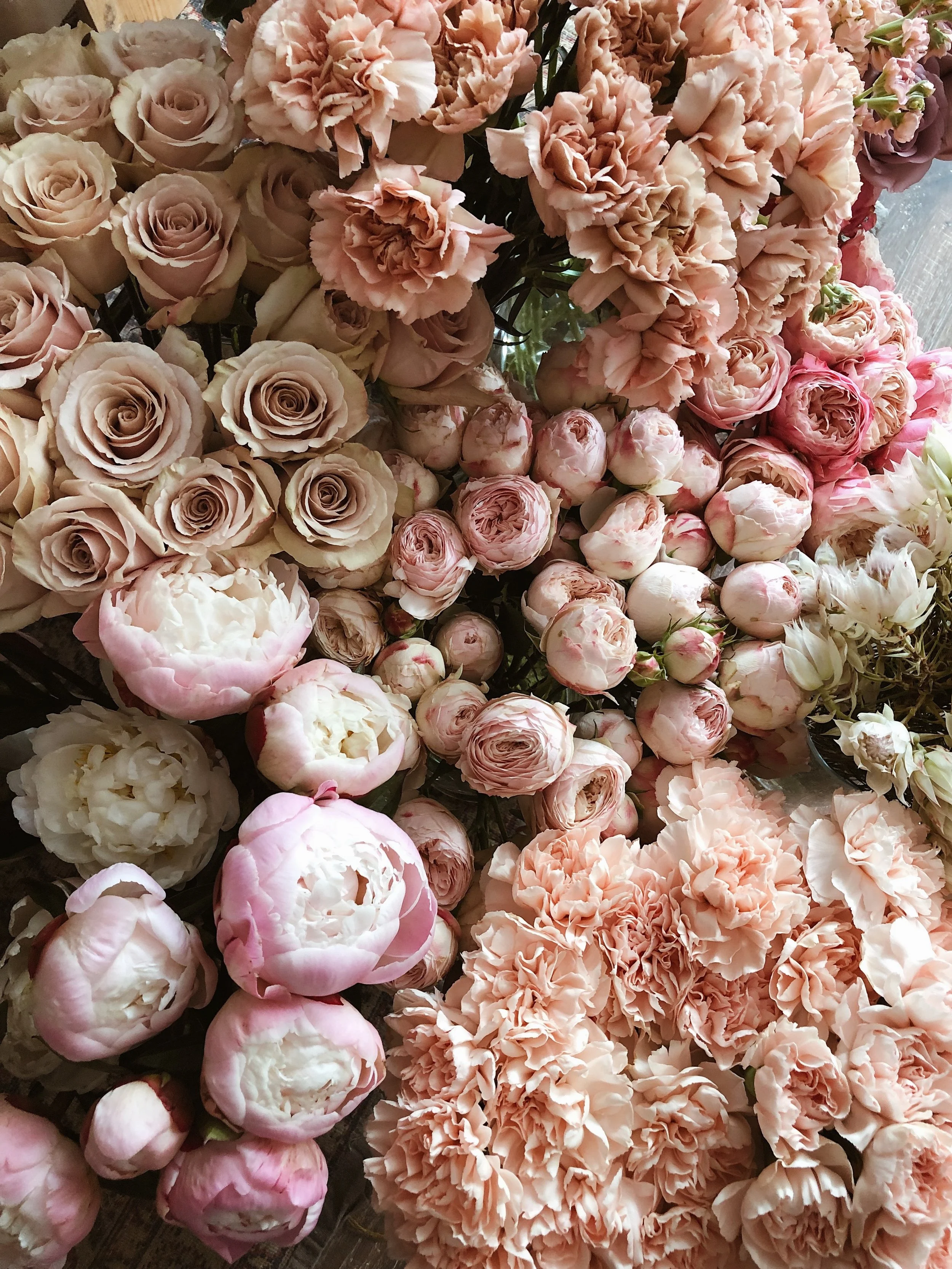 A variety of pink and cream roses, peonies, and carnations arranged closely together.