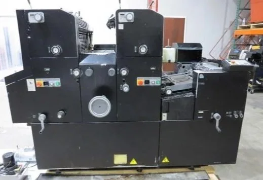 Industrial printing press with various control panels, switches, and rollers within a print shop.