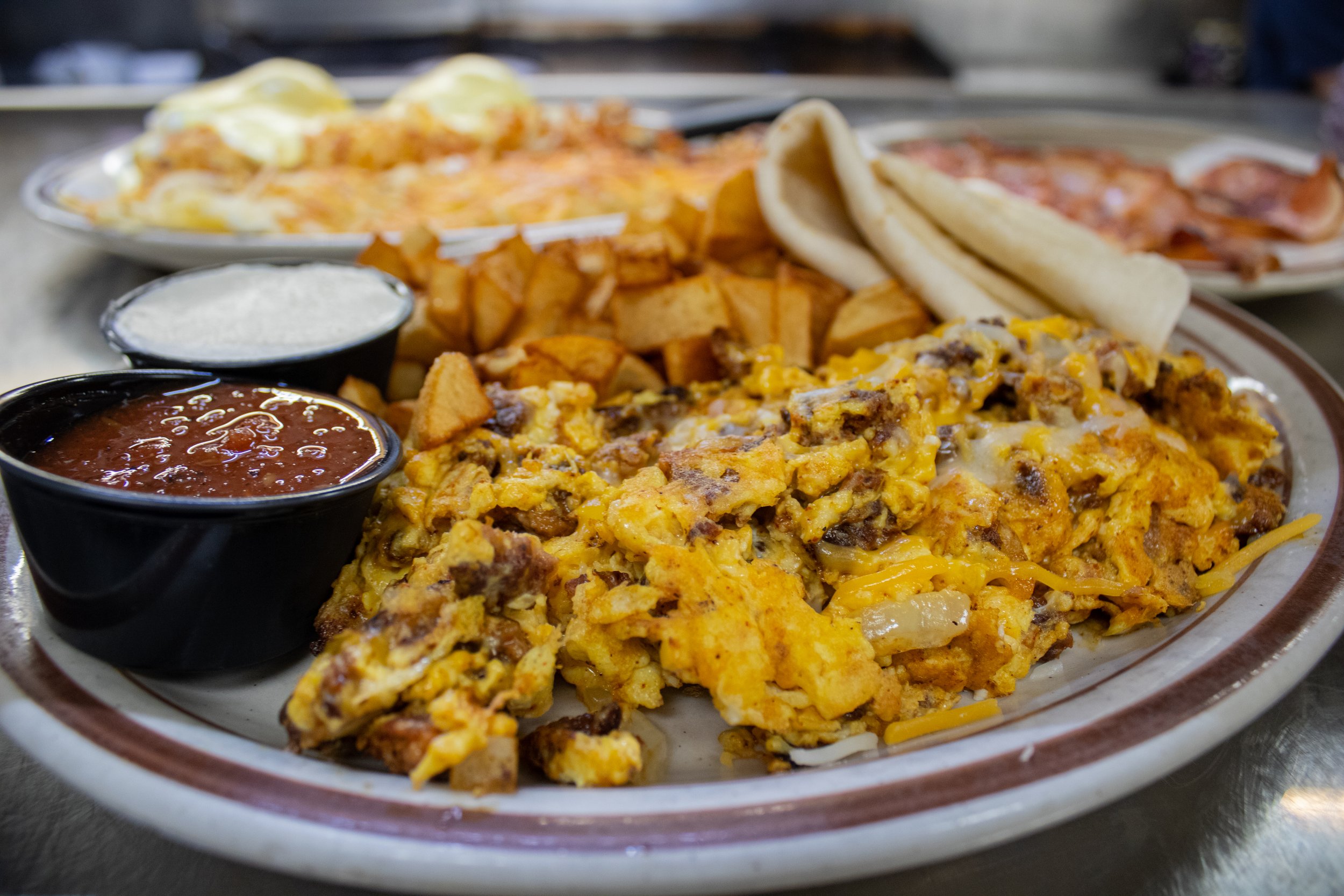 A photo of the twisted sister scramble with Glondo's sausage at the Sunset Cafe and Loose Wolf Saloon. The scramble is plated with hashbrowns, salsa, sour cream, and flour tortillas.