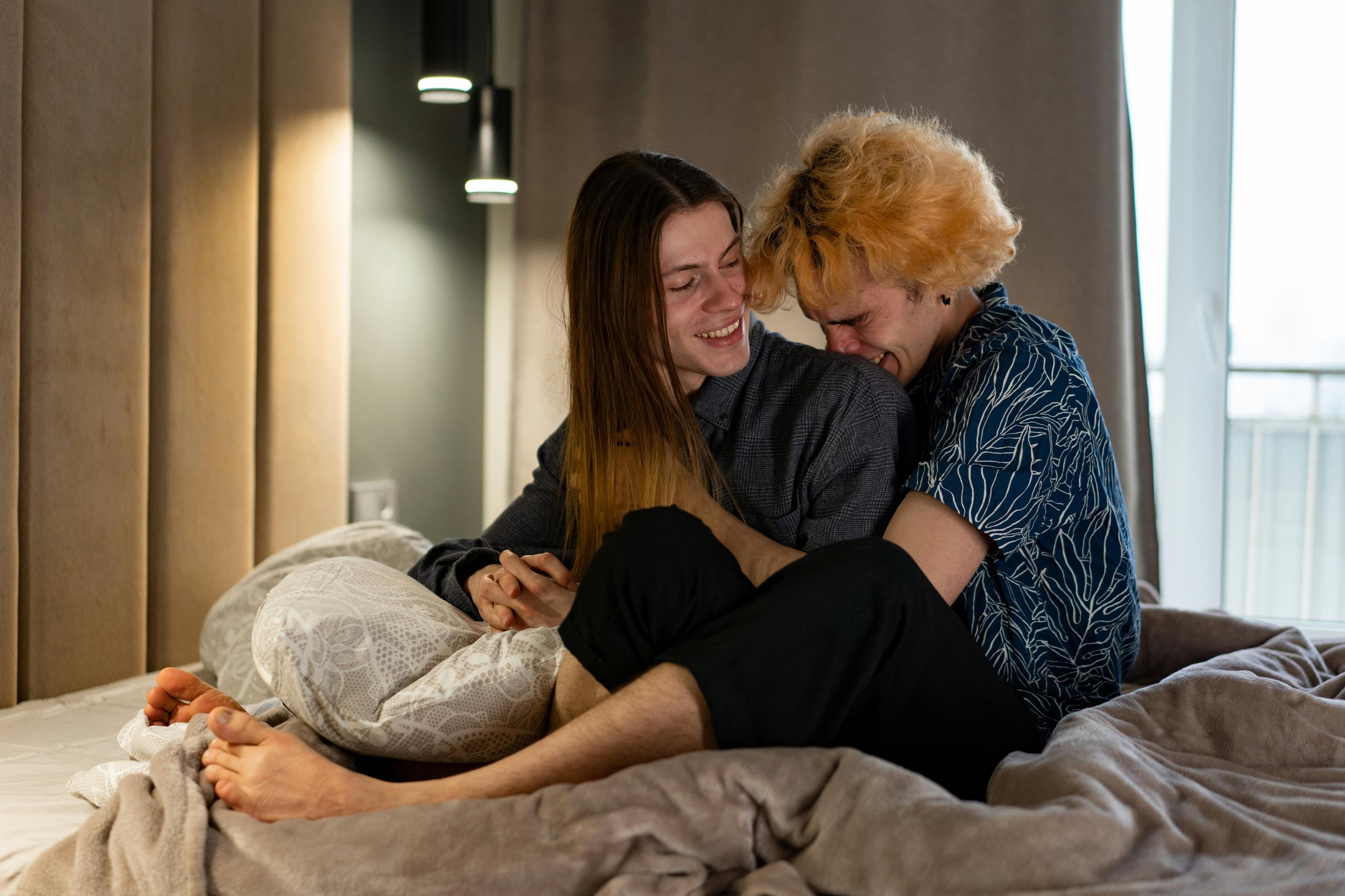 Image of a trans coupe laughing and hugging in bed