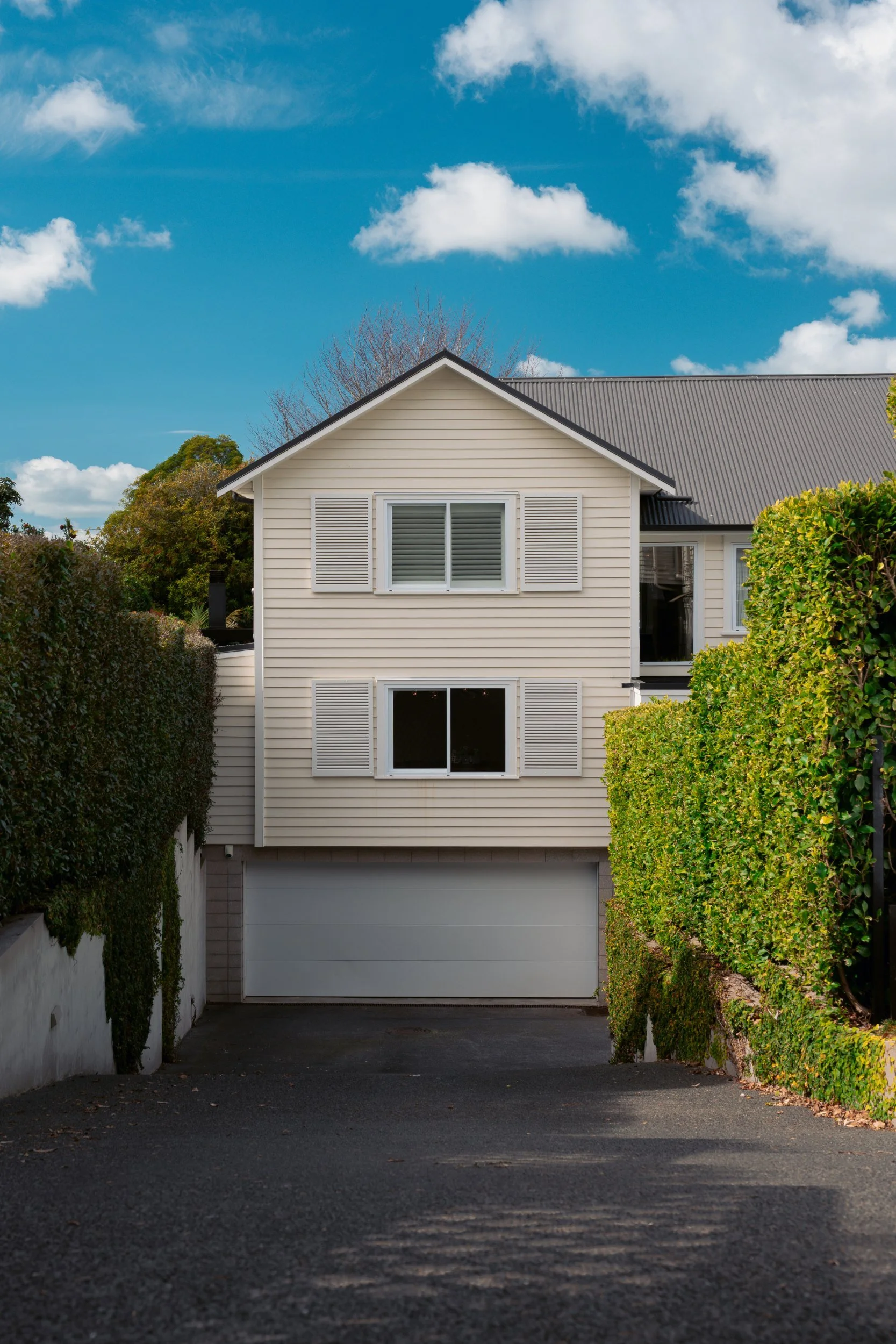 Completed white two-storey home with garage and established gardens, an architecturally designed home by The Bridge, Auckland