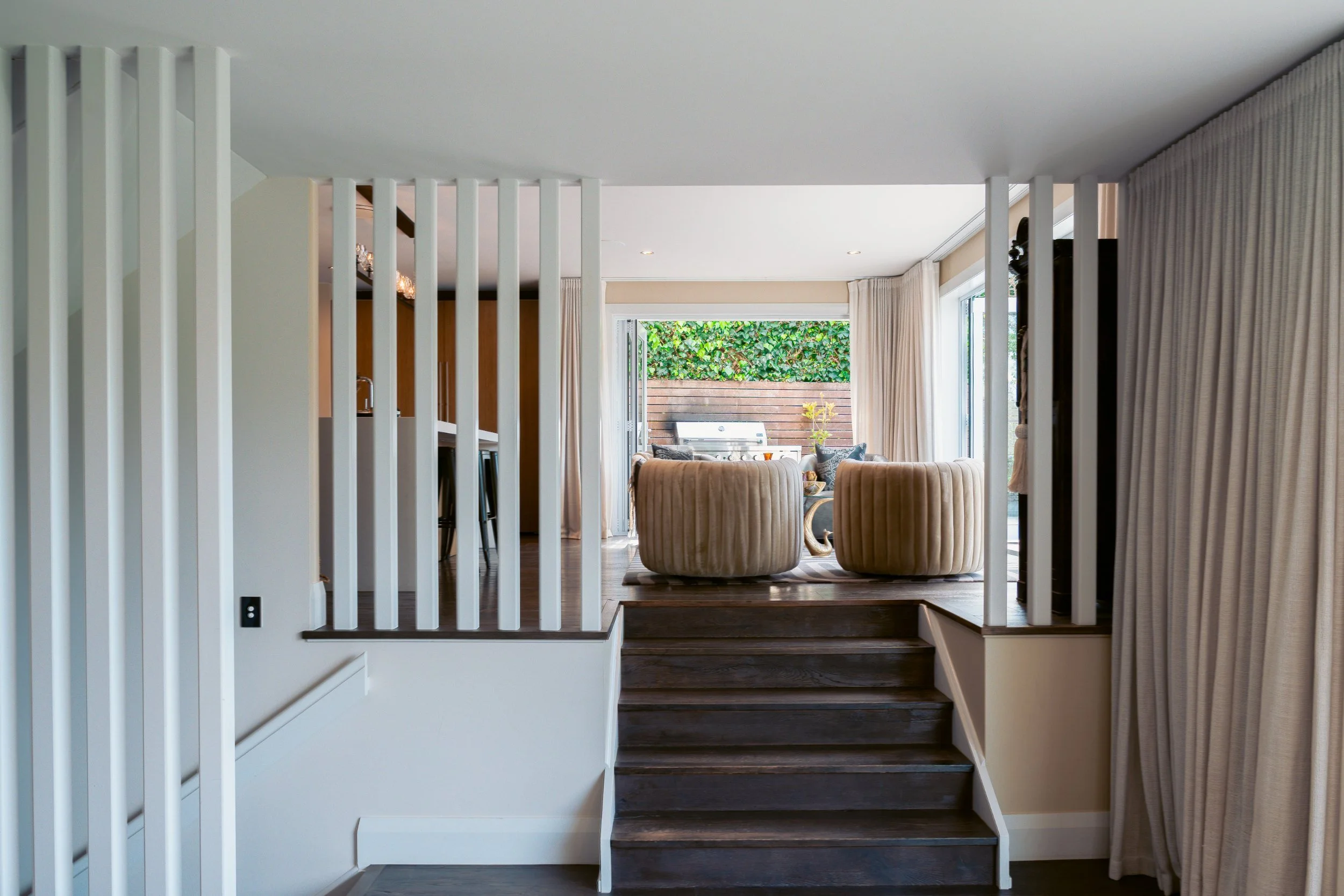 Staircase opening onto a sunlit living room with garden views in a luxury home by The Bridge, Auckland