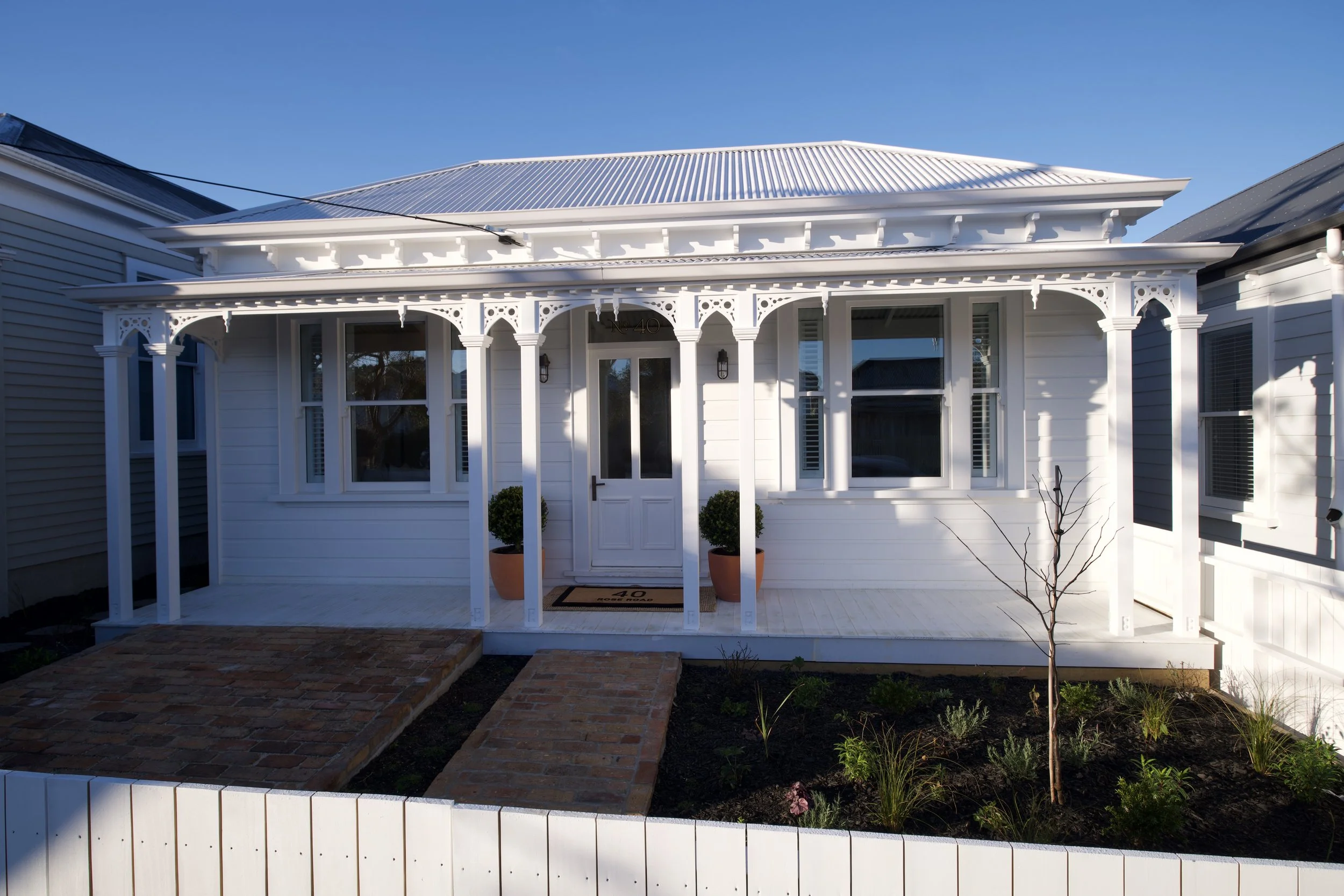 White heritage villa with decorative fretwork, veranda and brick path after a premium villa renovation by The Bridge, Auckland