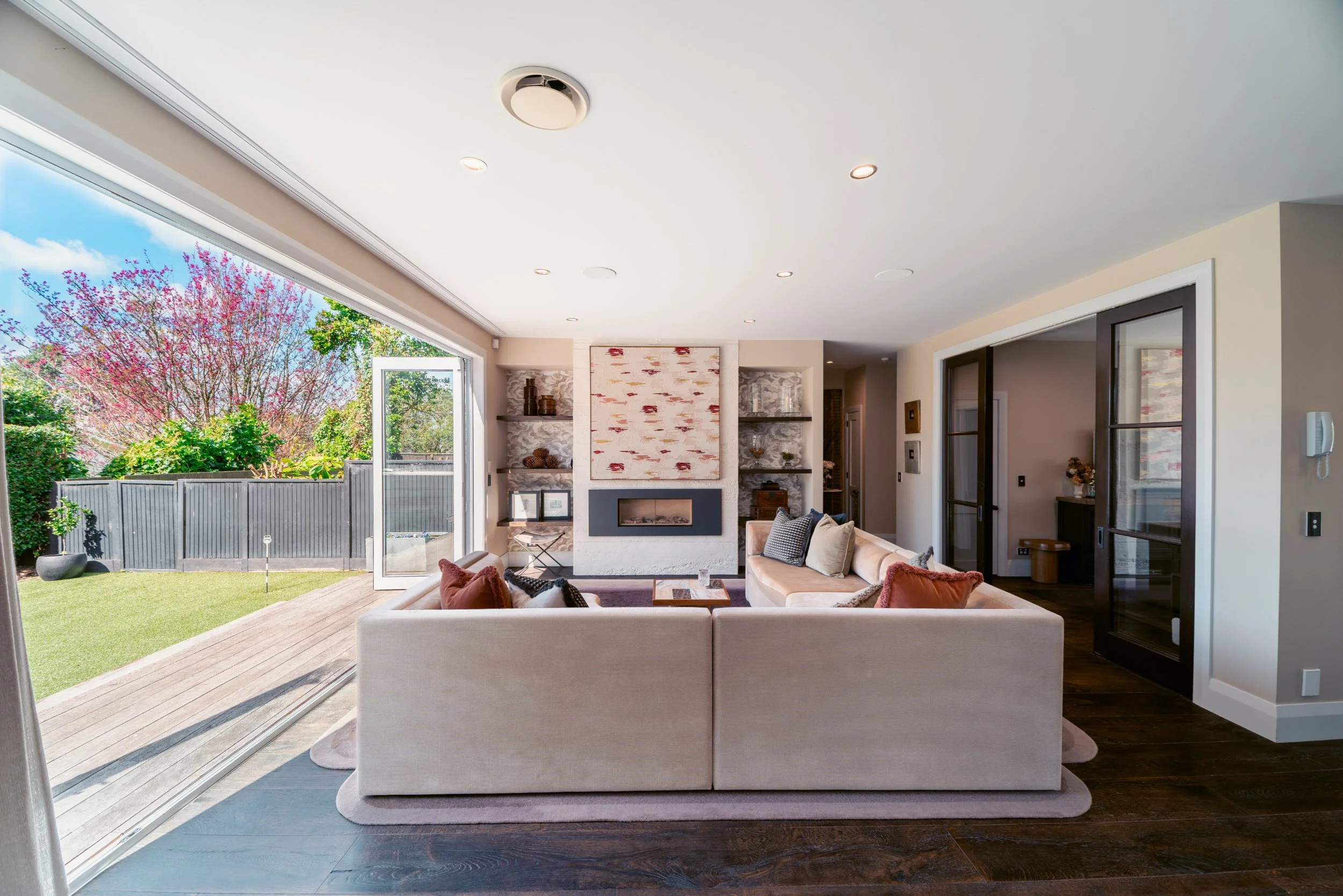 Light-filled living room with fireplace, built-in shelving and sliding doors to the garden in a luxury home renovation by The Bridge, Auckland