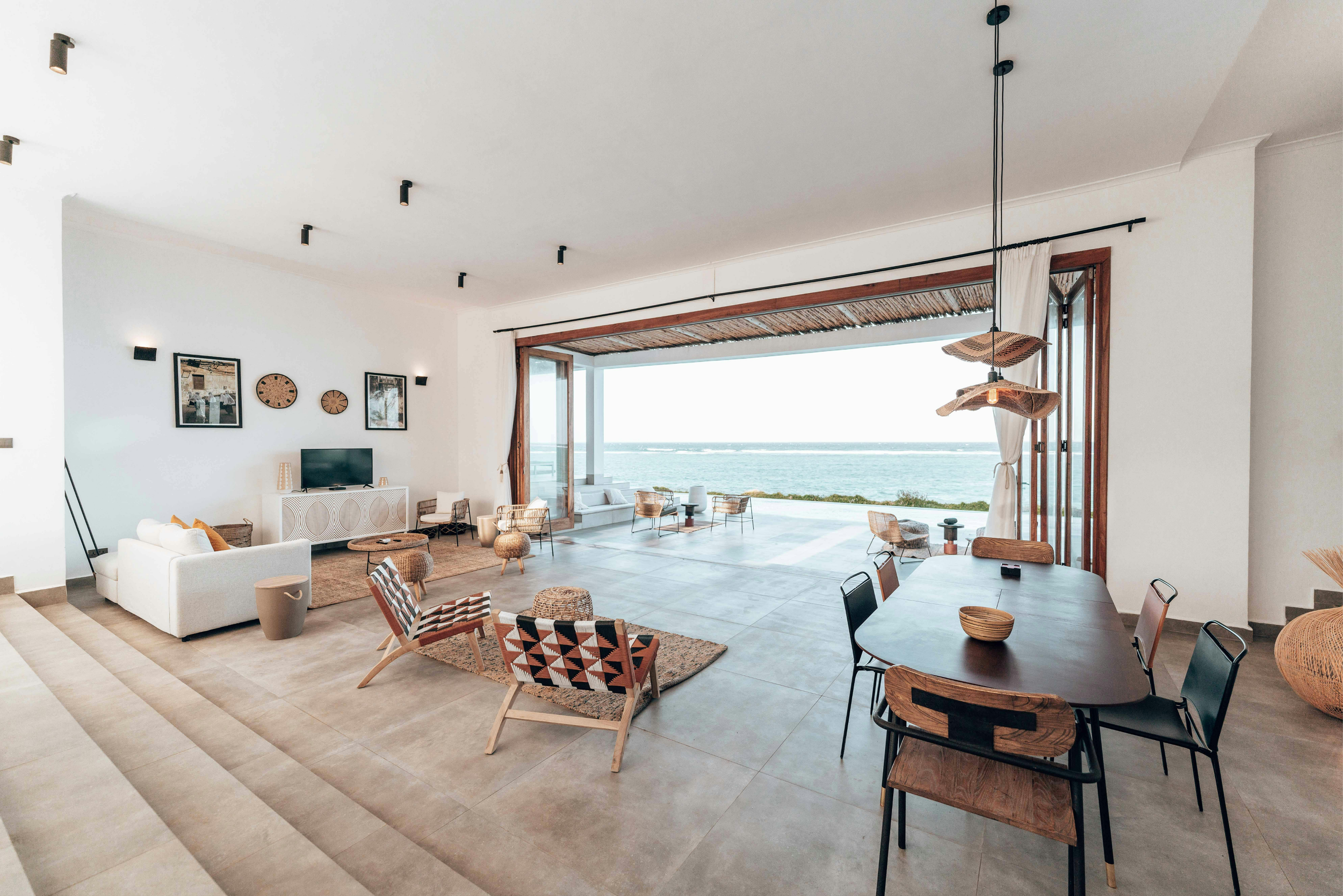 Open living room and dining area with large sliding doors leading to ocean view, modern furniture, and minimalist decor.