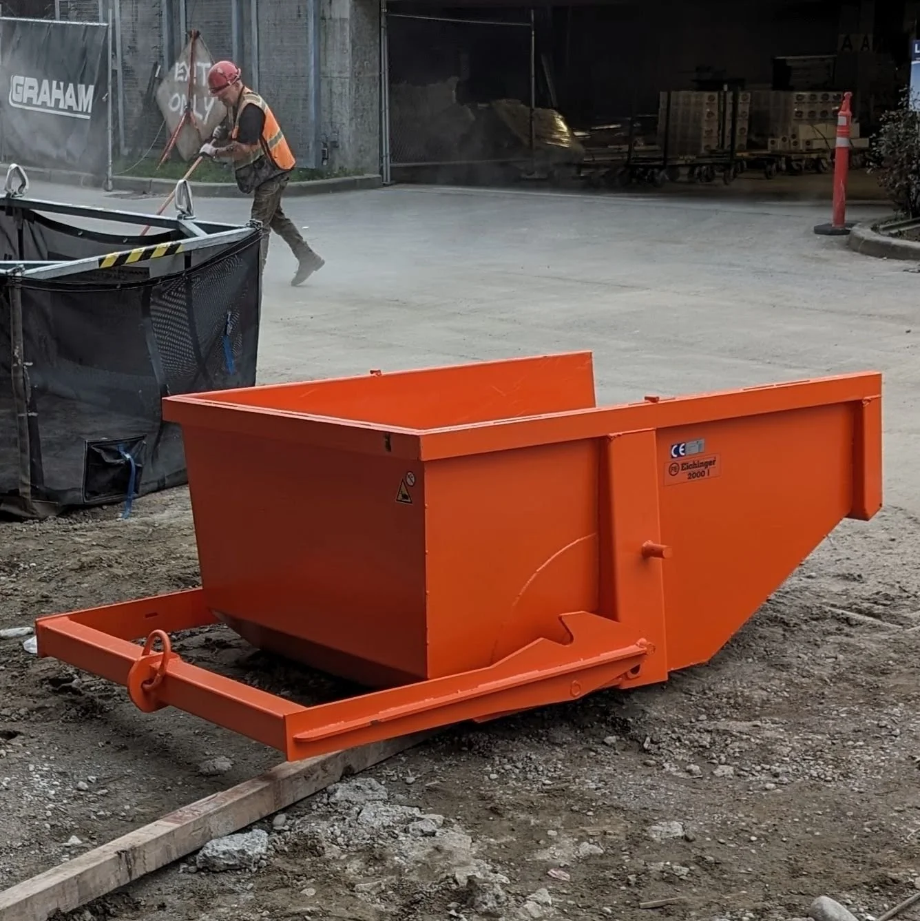 Skip Pan Hook lifting devices from Eichinger. These skip boxes are durable. This one is orange on a construction job site.