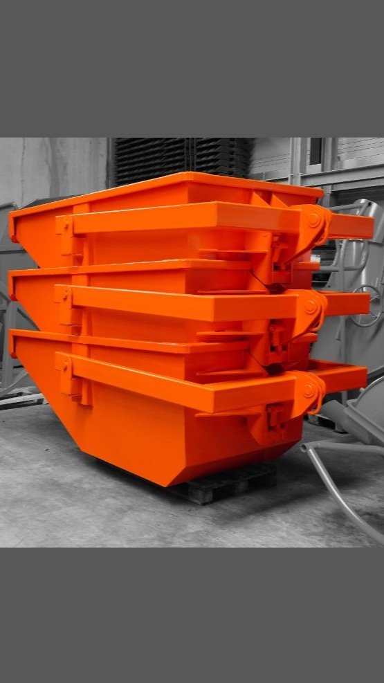 Tower Crane Trash Bin in orange ready to ship as a stack of three. The bins are orange with a desaturated background inside of the factory storage.