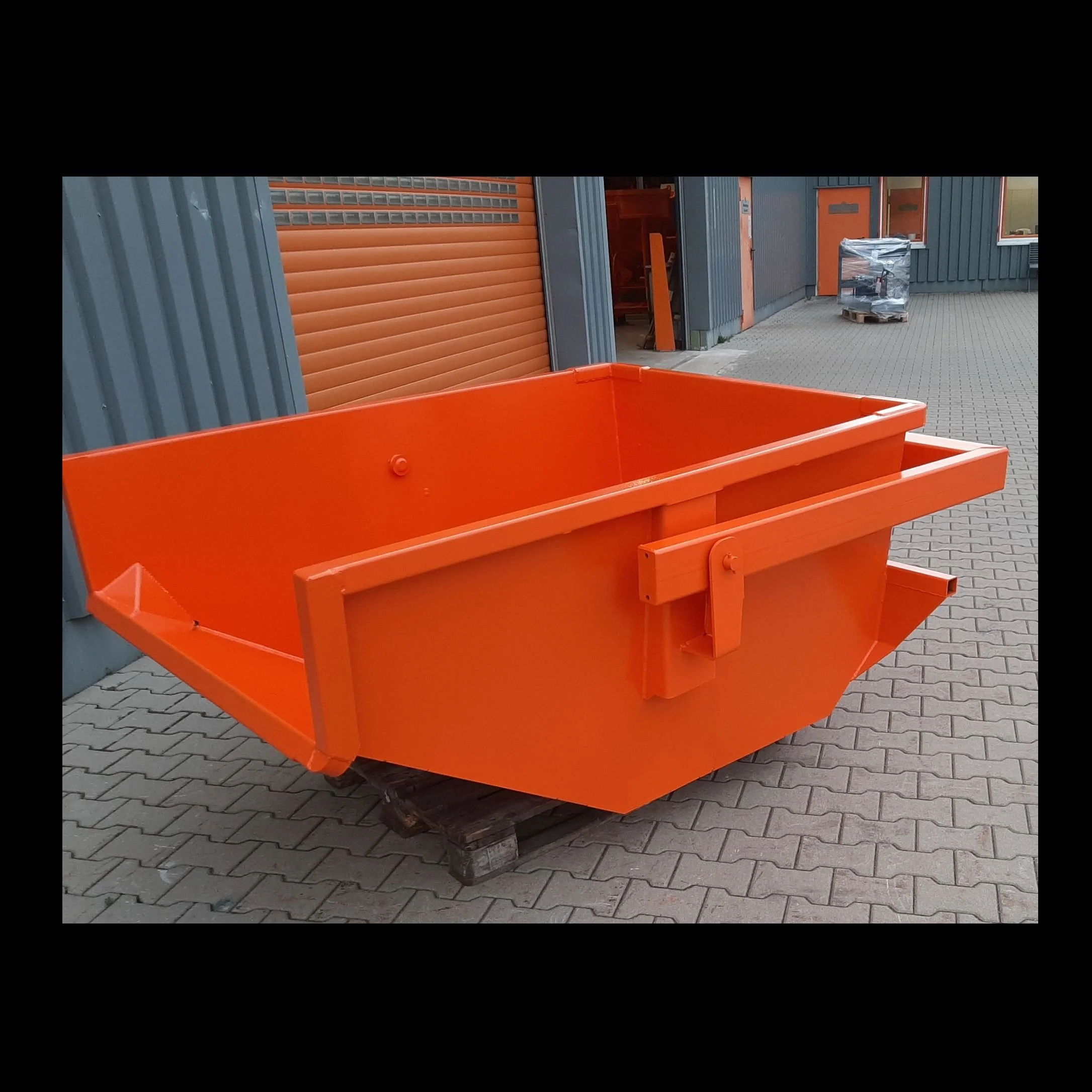Eichinger Crane Skip Pan without forklift pockets at the factory. The pan is in orange and sitting on a block driveway at the factory.