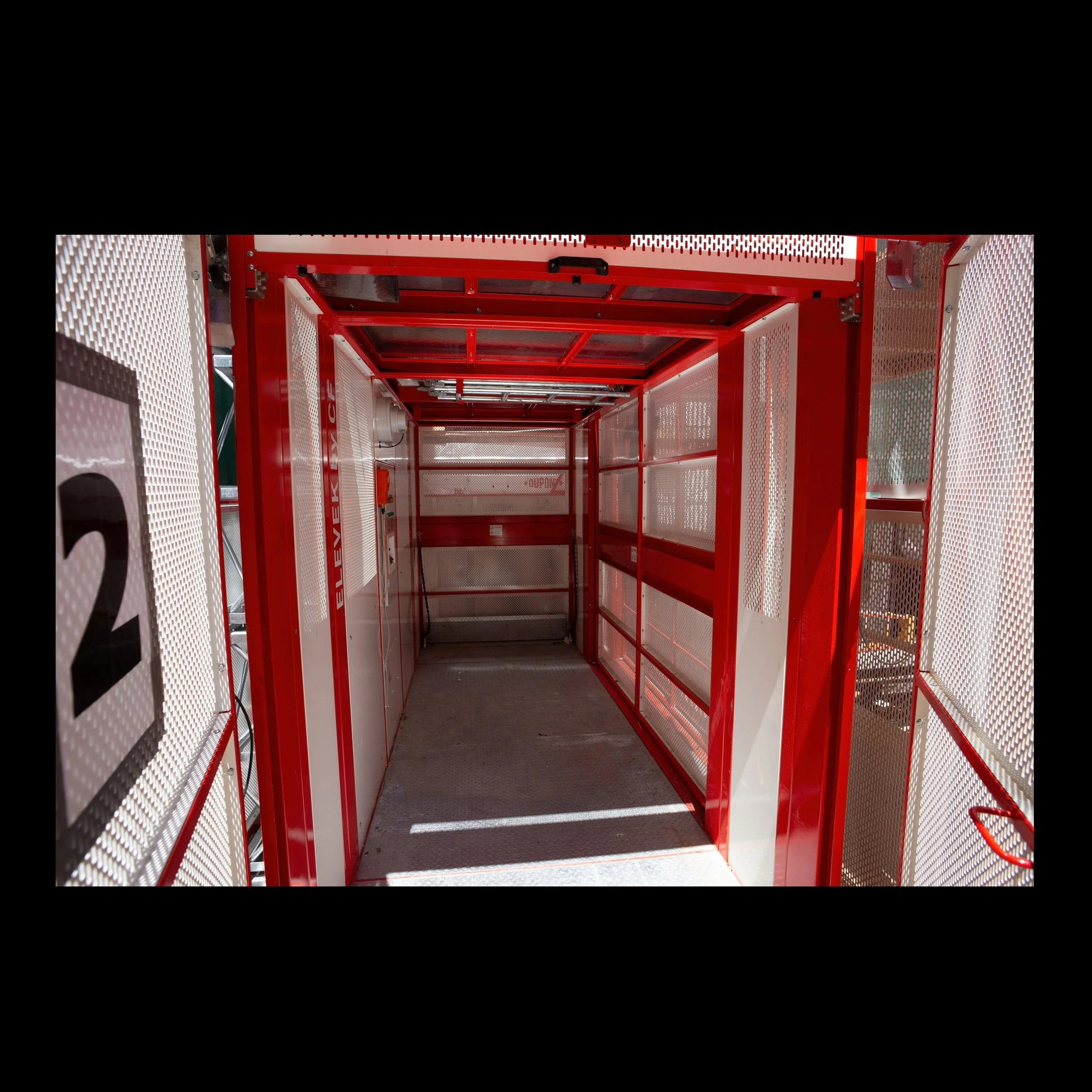 Efficiency in safely transporting workers is achived in this red an white construction hoist. The cabin of the plat form is shown in the picture.