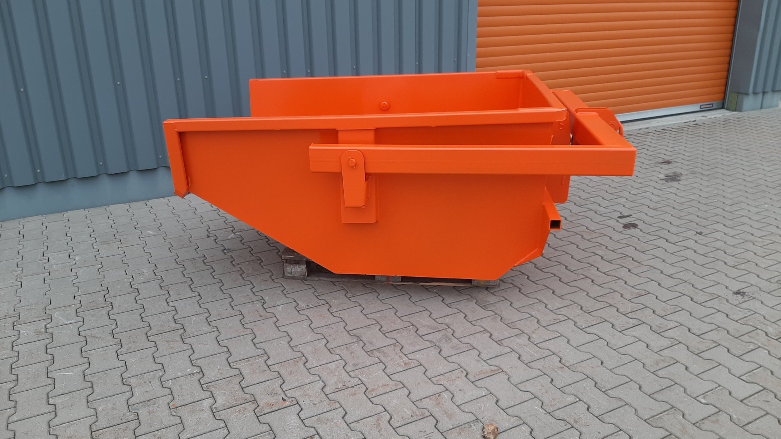 Automatic Crane Trash Skip in Orange by Eichinger of Germany. The background is the factory wall with the skip sitting on gray bricks