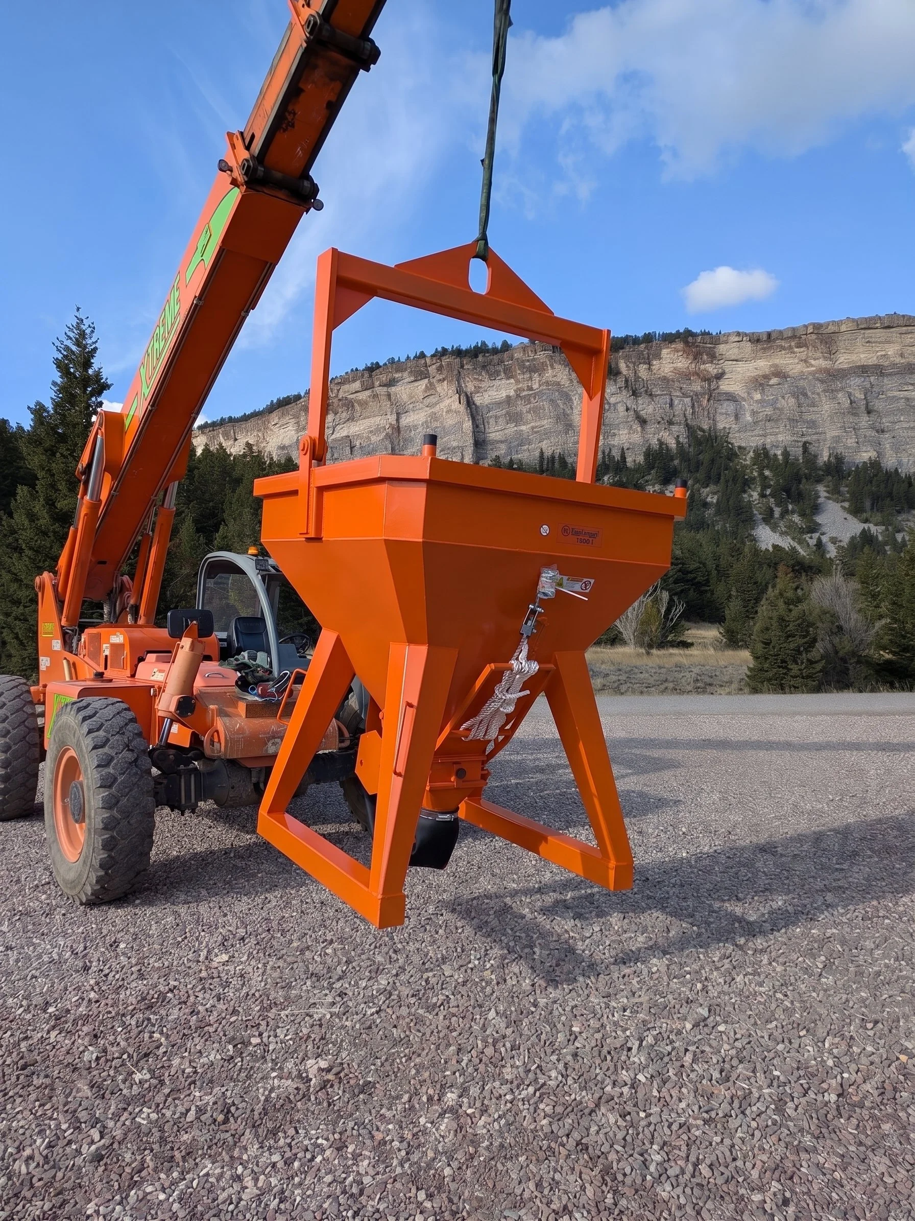 Concrete Bucket Model 1035 by Eichinger from CraneGear. It's Orange and hanging from a telehandler forklift. The background is Glacier National Park.