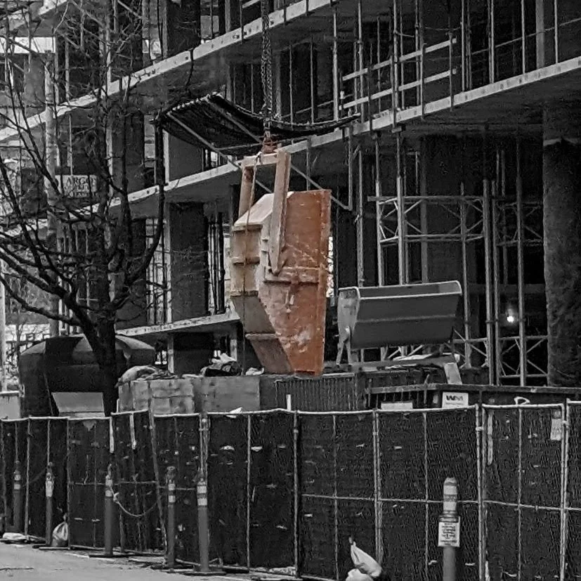 Hook lifting devices by Eichinger at some of the best in the world. This skip pan is being dumped out and is vertical. It's brown and on a job site that has been rendered black and white.