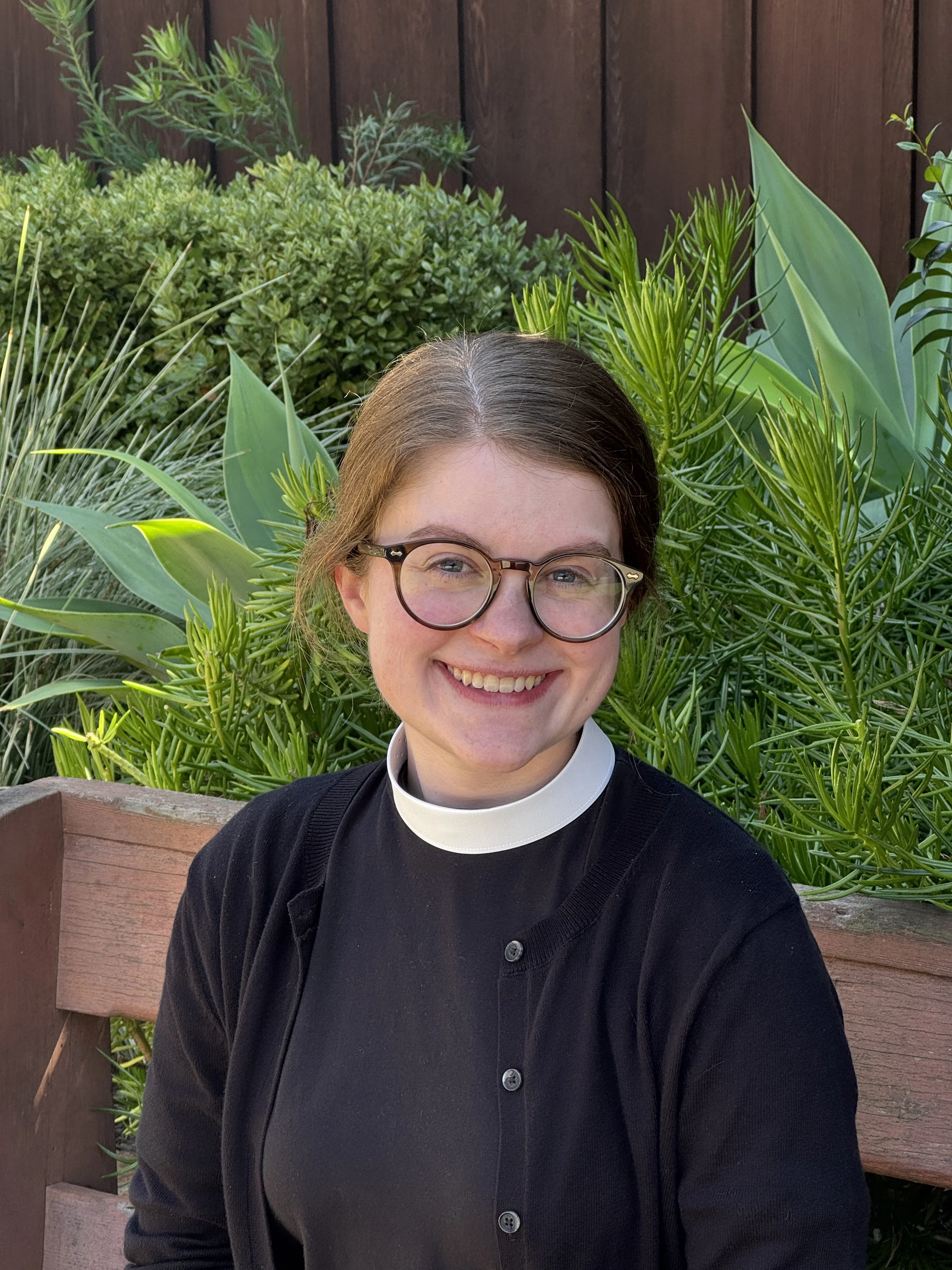 A young woman with long, wavy brown hair, blue eyes, and a broad smile, wearing a black top.