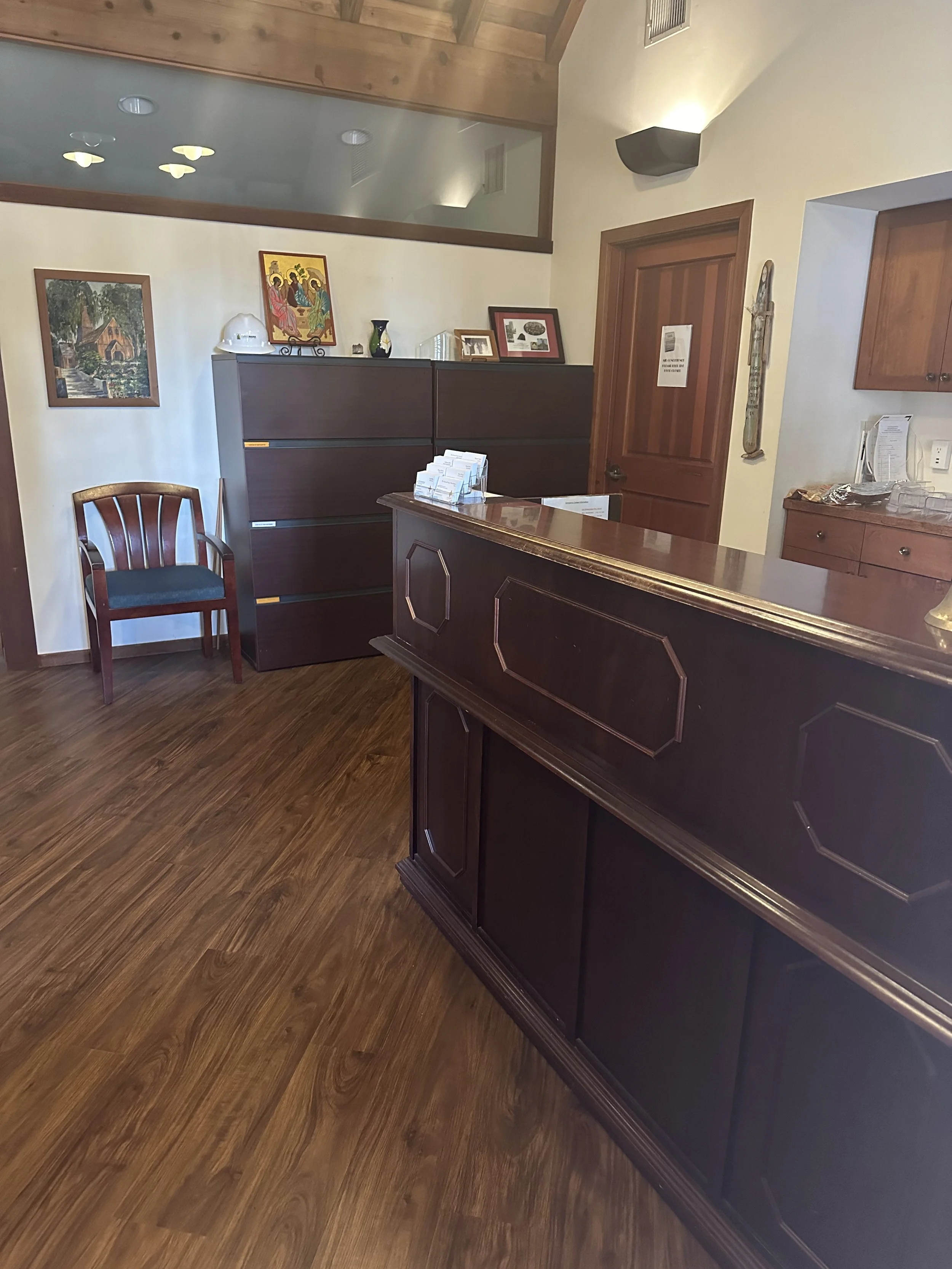 Reception area with dark wood furniture, including a cabinet and a reception desk, a wooden chair, and decorative artwork on the walls.