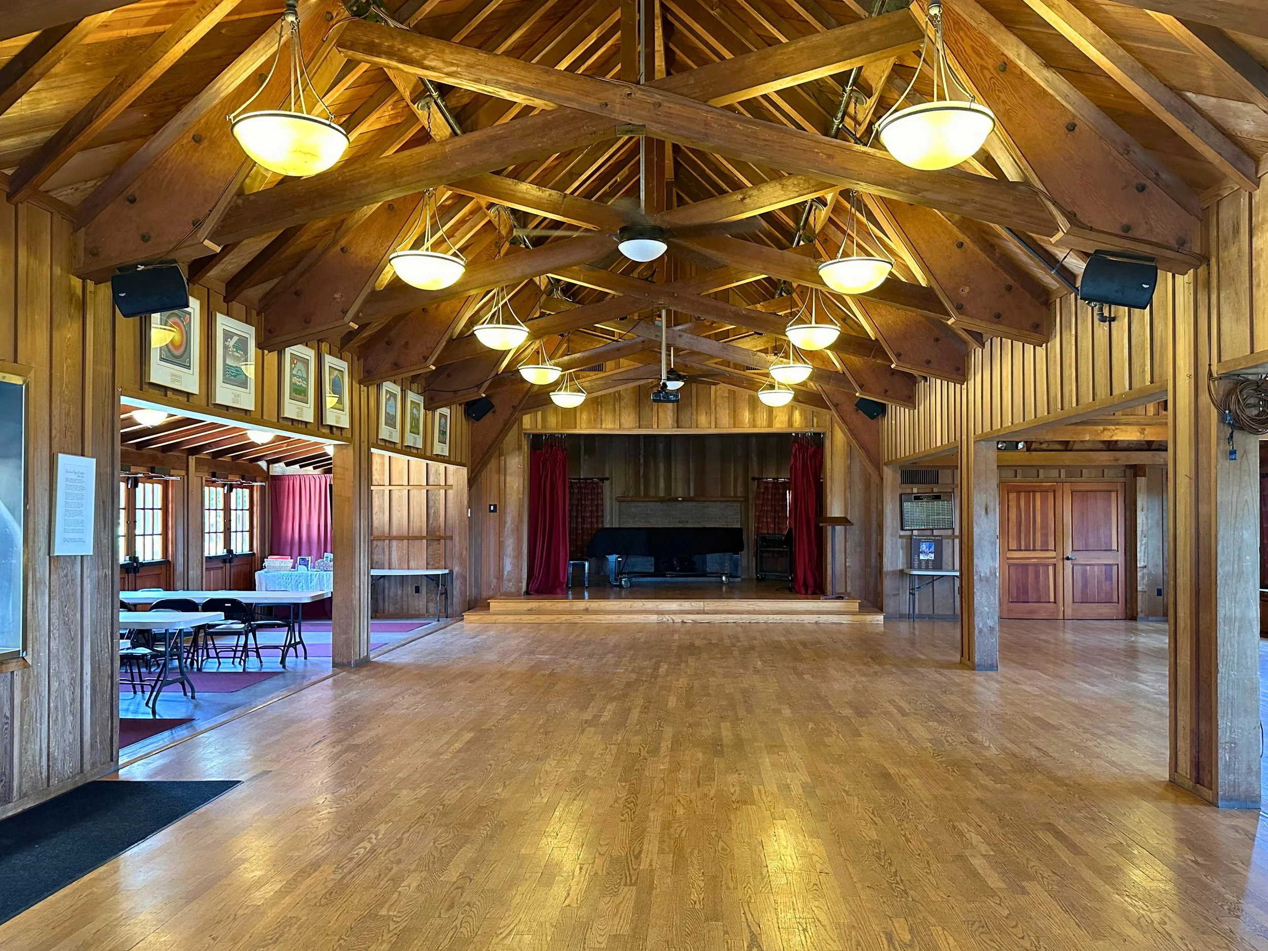 Small wooden auditorium with stage, red curtains, ceiling lights, and wooden beams.
