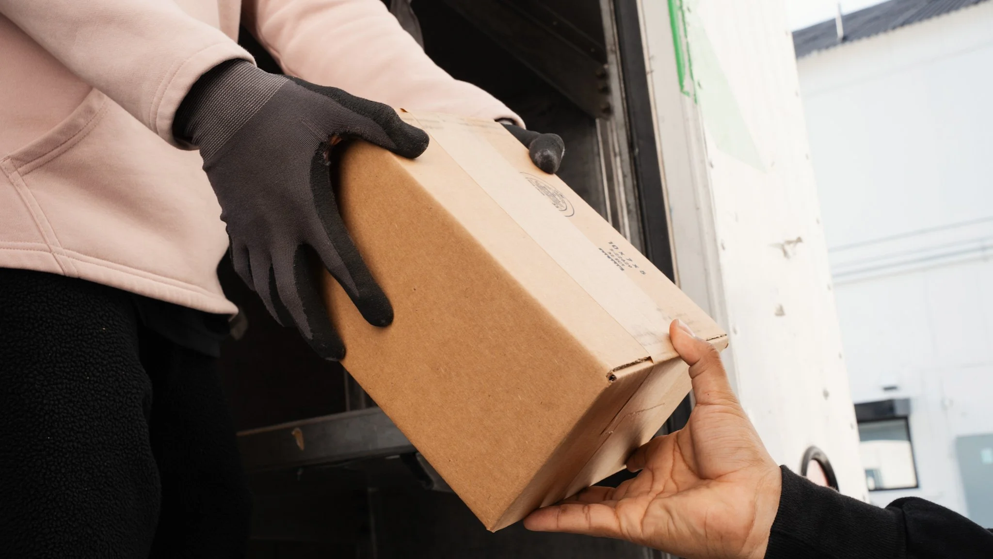 Person in pink hoodie handing cardboard box to another person outside a truck door.