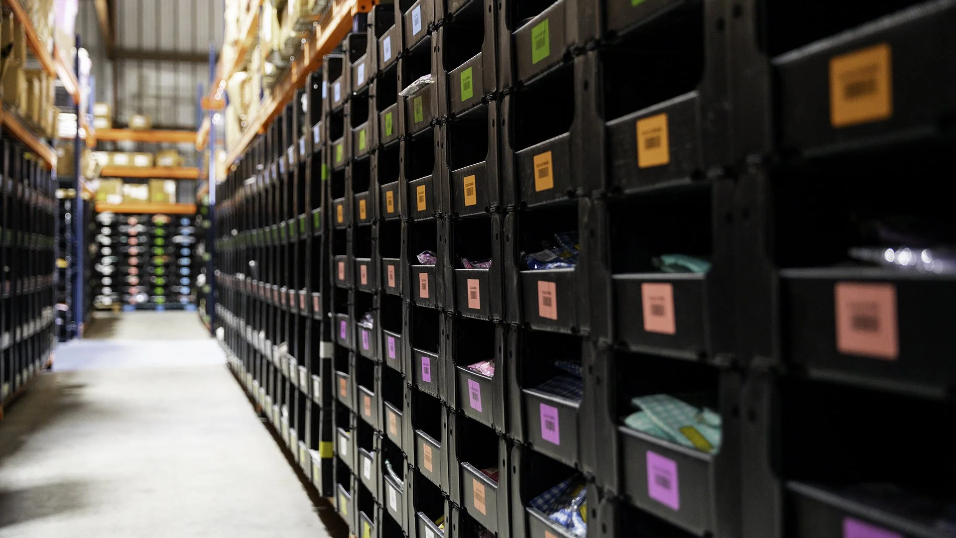 Warehouse aisle with shelves of labeled black bins