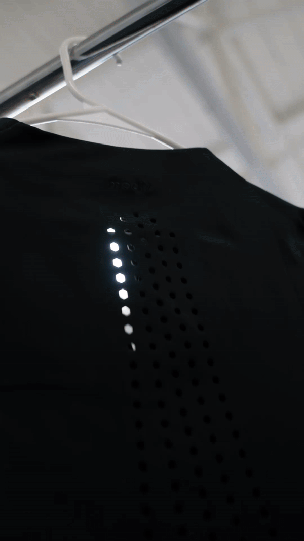 Black shirt with laser-cut ventilation holes hanging on a clothes hanger.