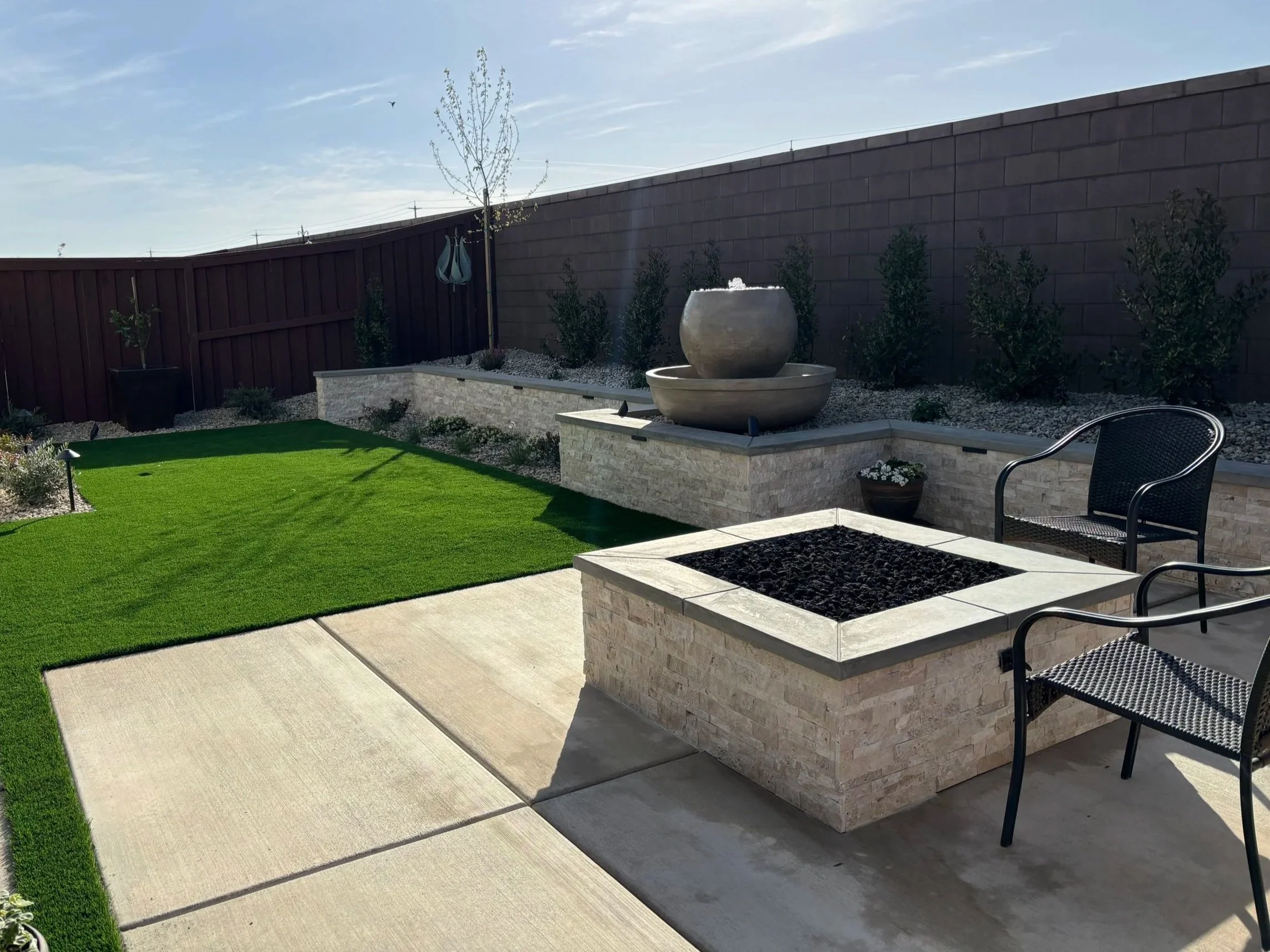 A backyard patio with synthetic turf, custom wall and  stone water fountain.