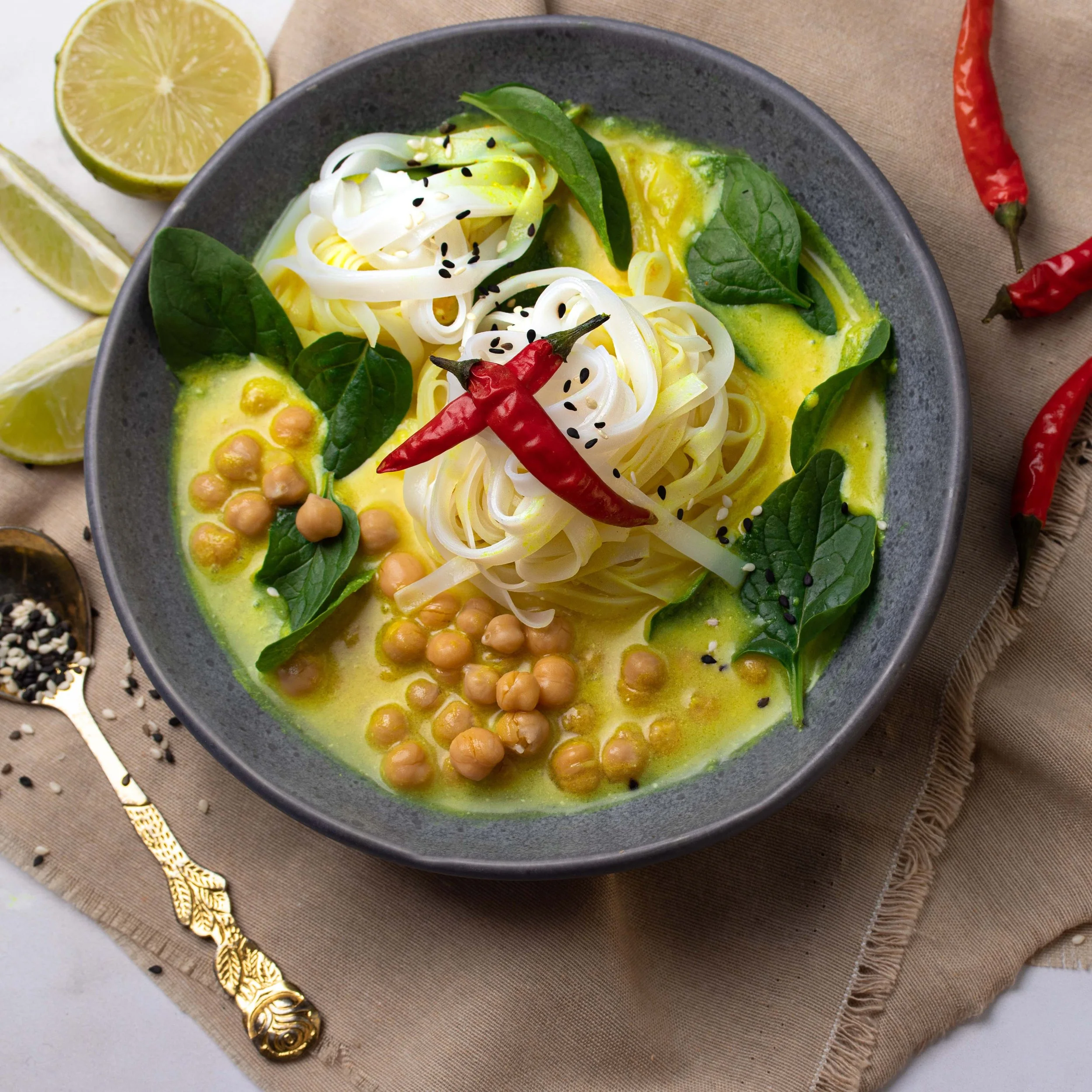 Vegan noodle soup with chickpeas, spinach, chili, and lemon halves on a beige cloth