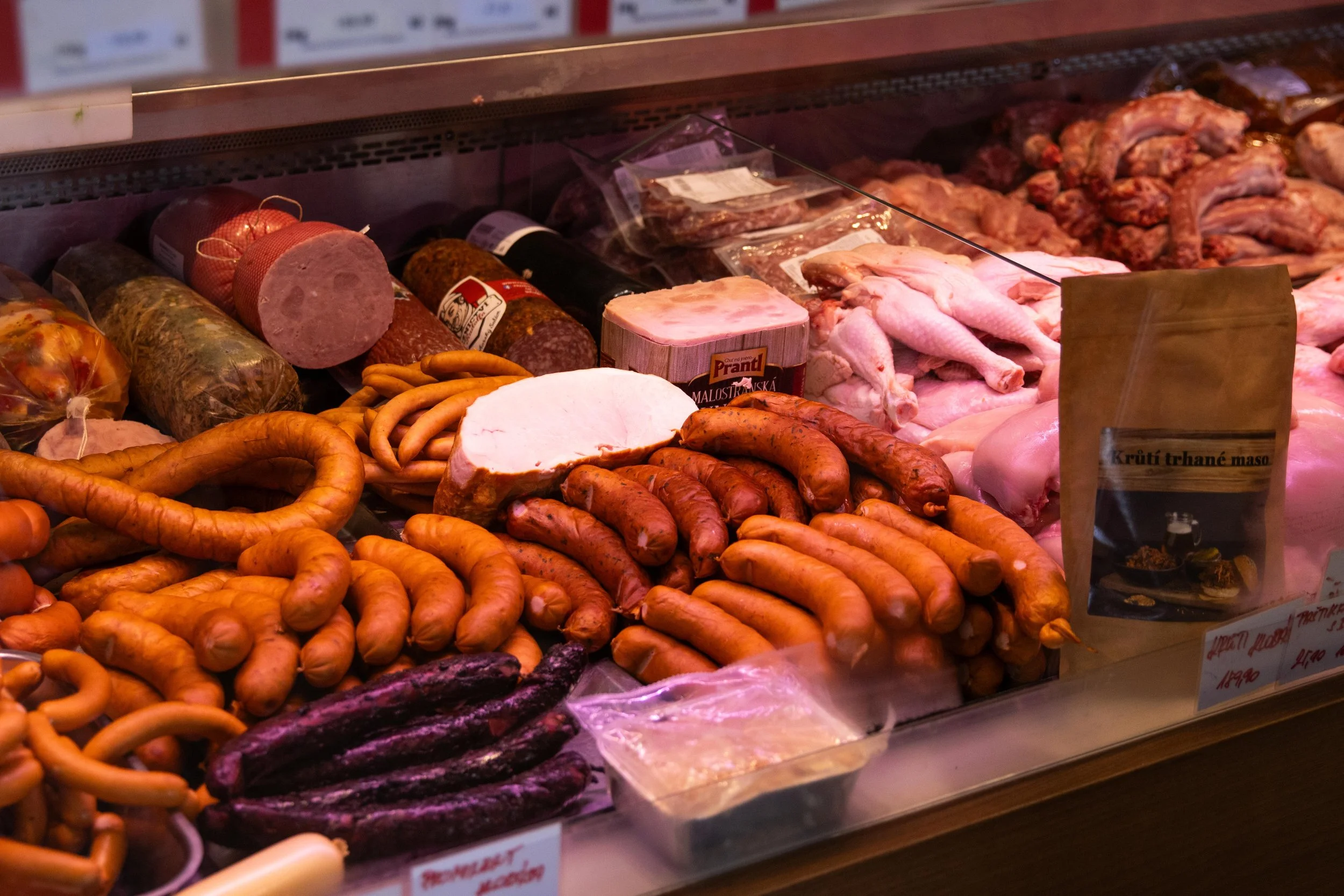 Display of various meats and sausages in a butcher shop, including sausages, ham, chicken, and other processed meat products.