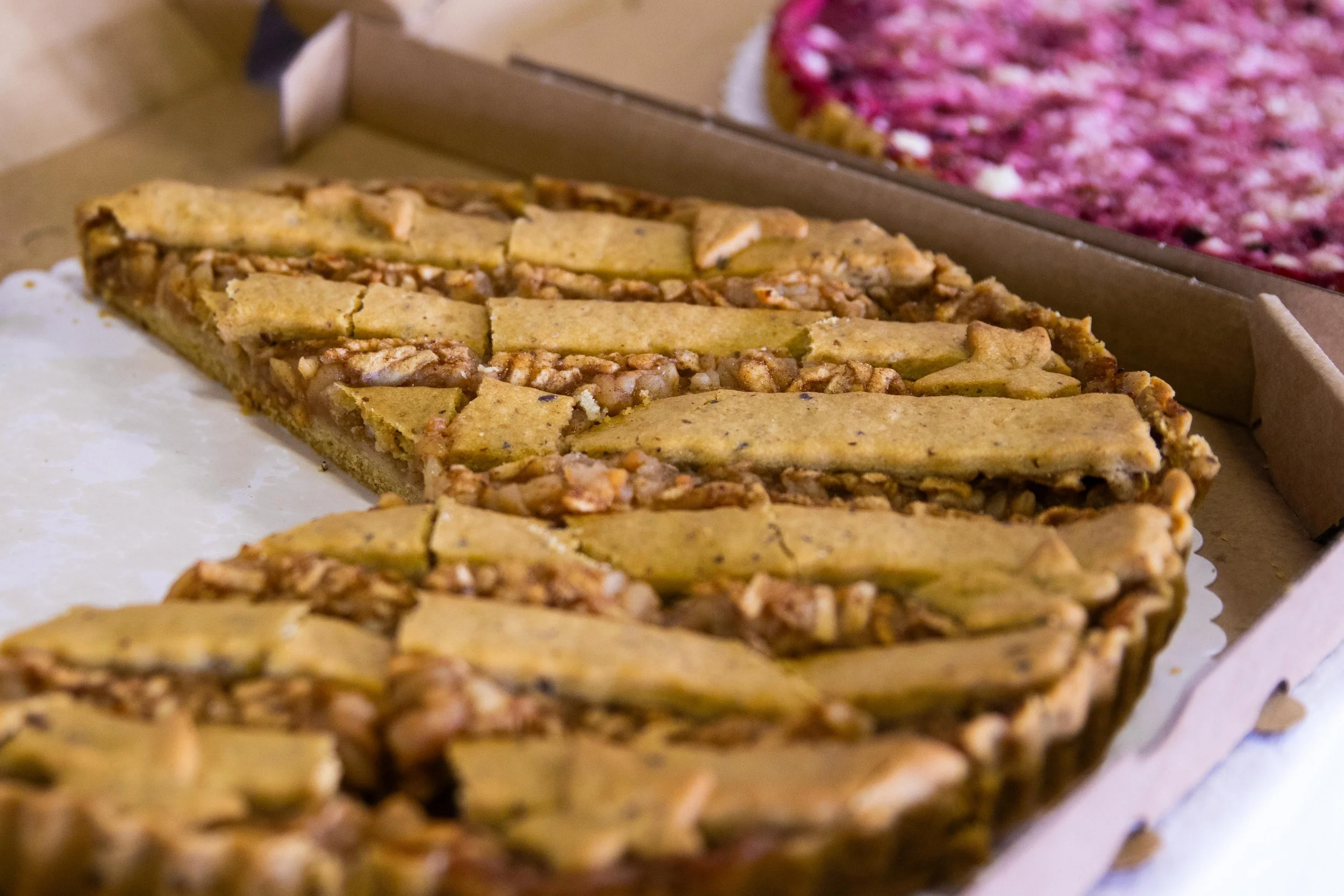 Close-up of pecan pie slices in a cardboard box with another dessert in a box in the background.