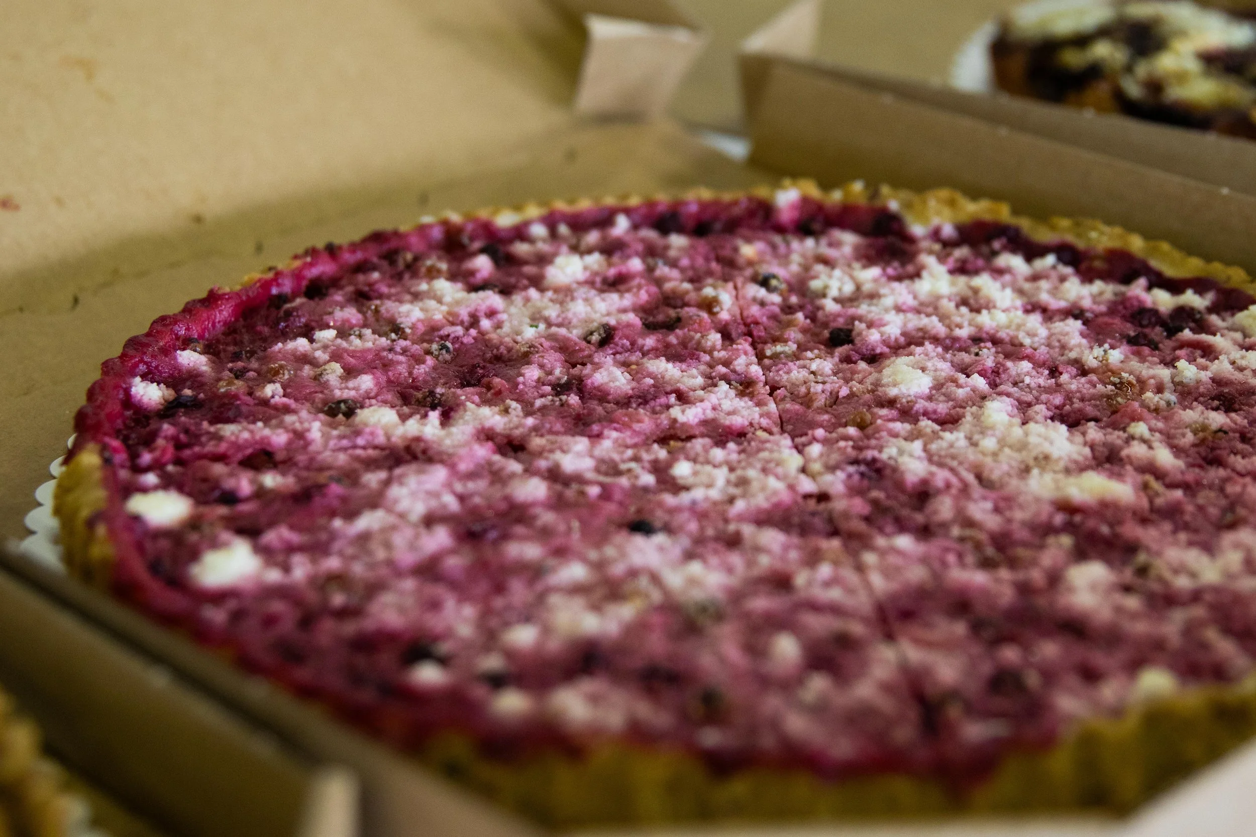 A freshly baked berry pie with a crumbly topping in an open cardboard box.