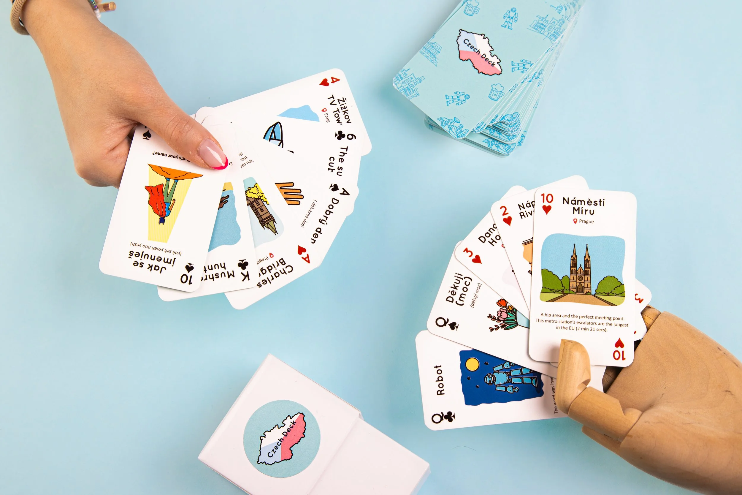 Playing cards featuring illustrations and descriptions of various locations in the Czech Republic, including Prague and the Czech Docks, are spread on a light blue surface. A deck box with a map of the Czech Docks is also visible.