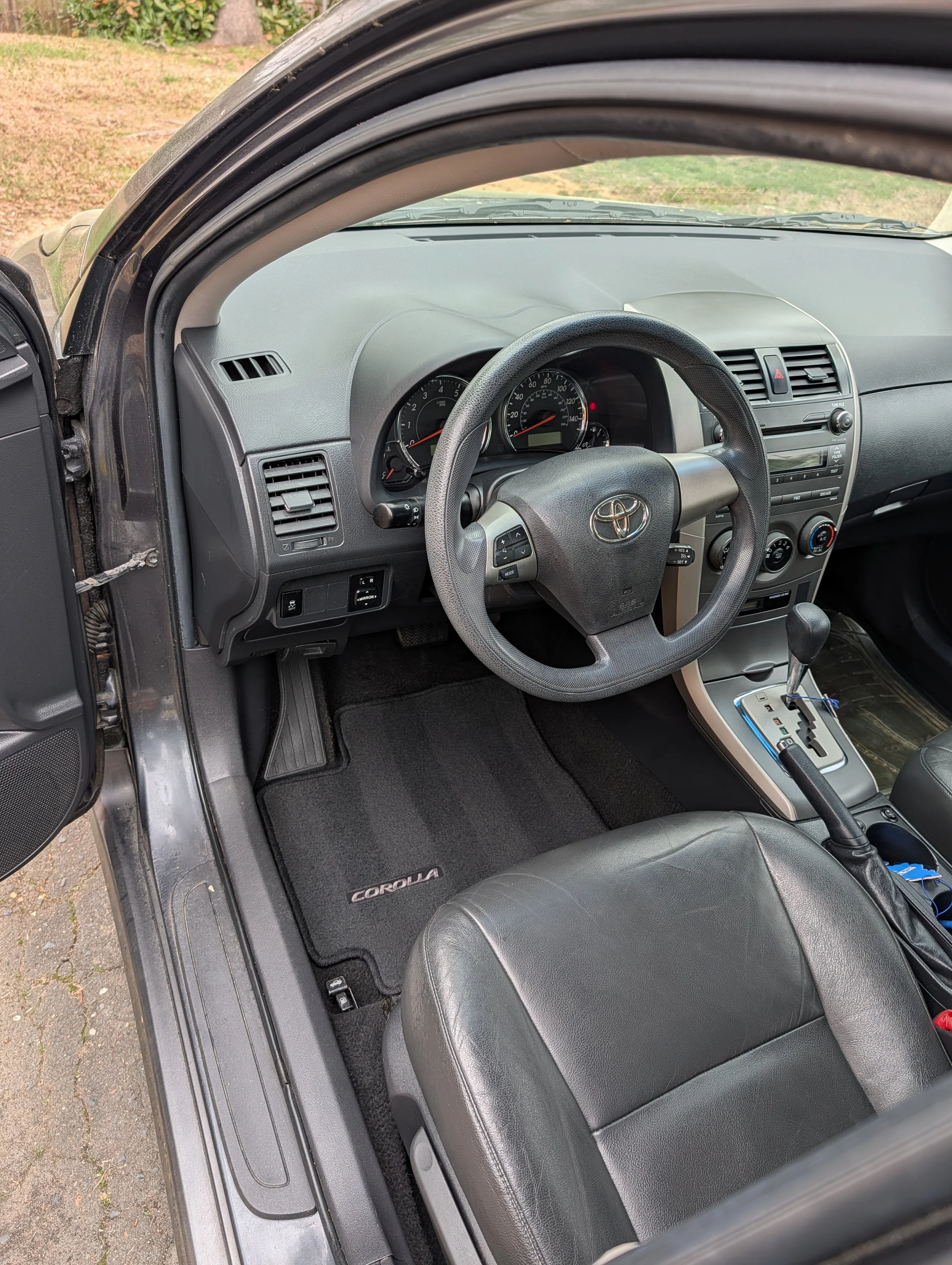 Interior of a Toyota Corolla, showing the steering wheel, dashboard, gear shift, and driver's seat.