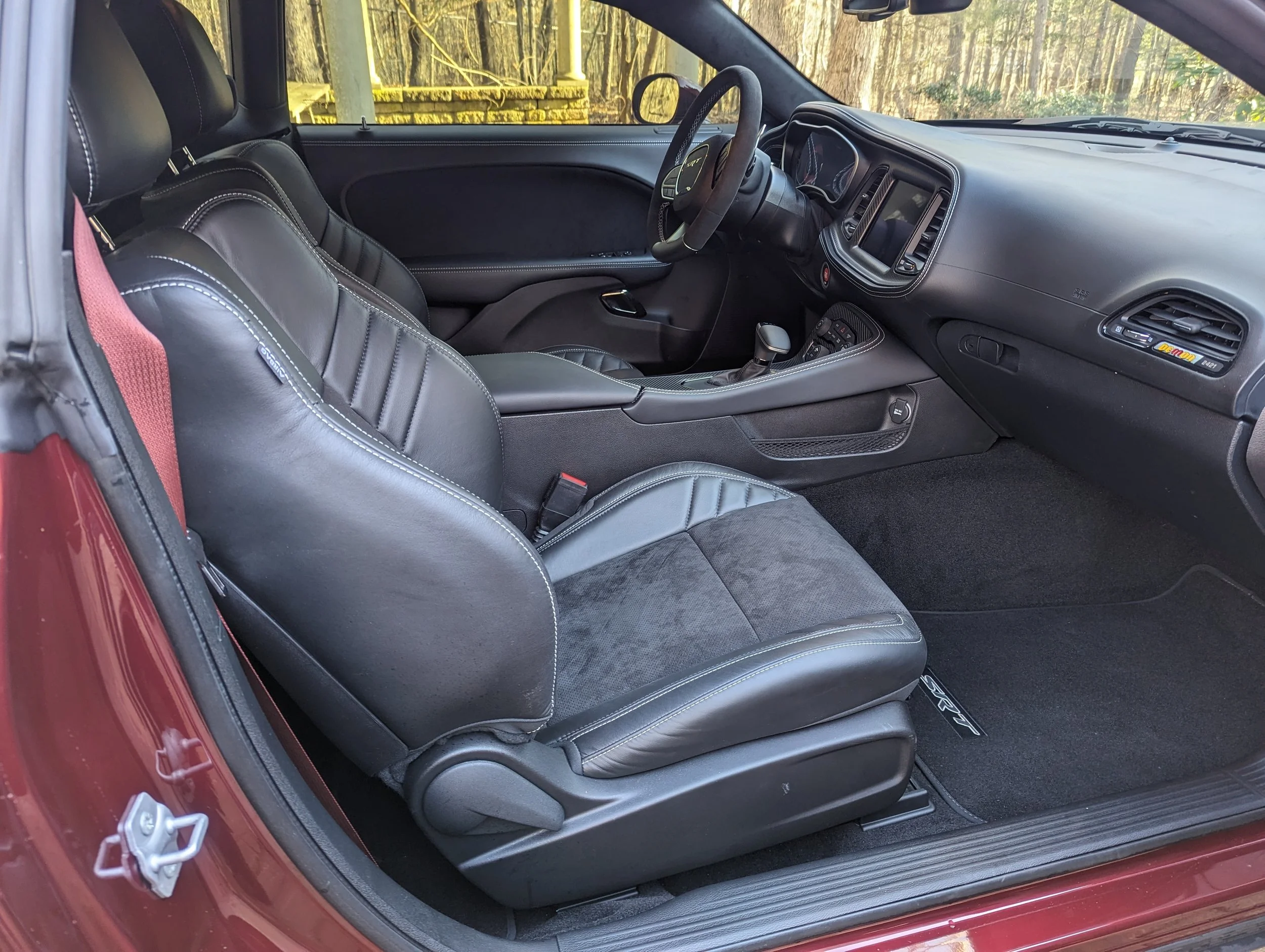 Interior of a red sports car with black leather seats, dashboard, and center console, featuring a manual transmission and a view of the wooded area outside through the windshield.