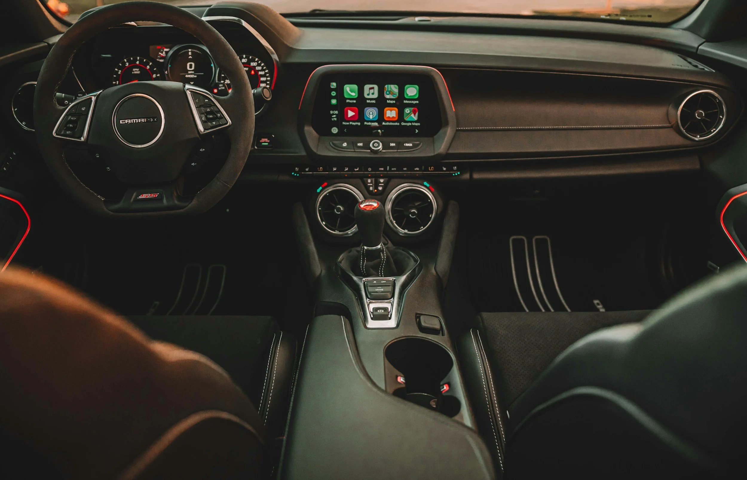 Inside view of a car dashboard showing a touchscreen display with apps like Phone, Music, Maps, Messages, YouTube, Podcasts, Audiobooks, Google Maps, and a gear shift in the center console.