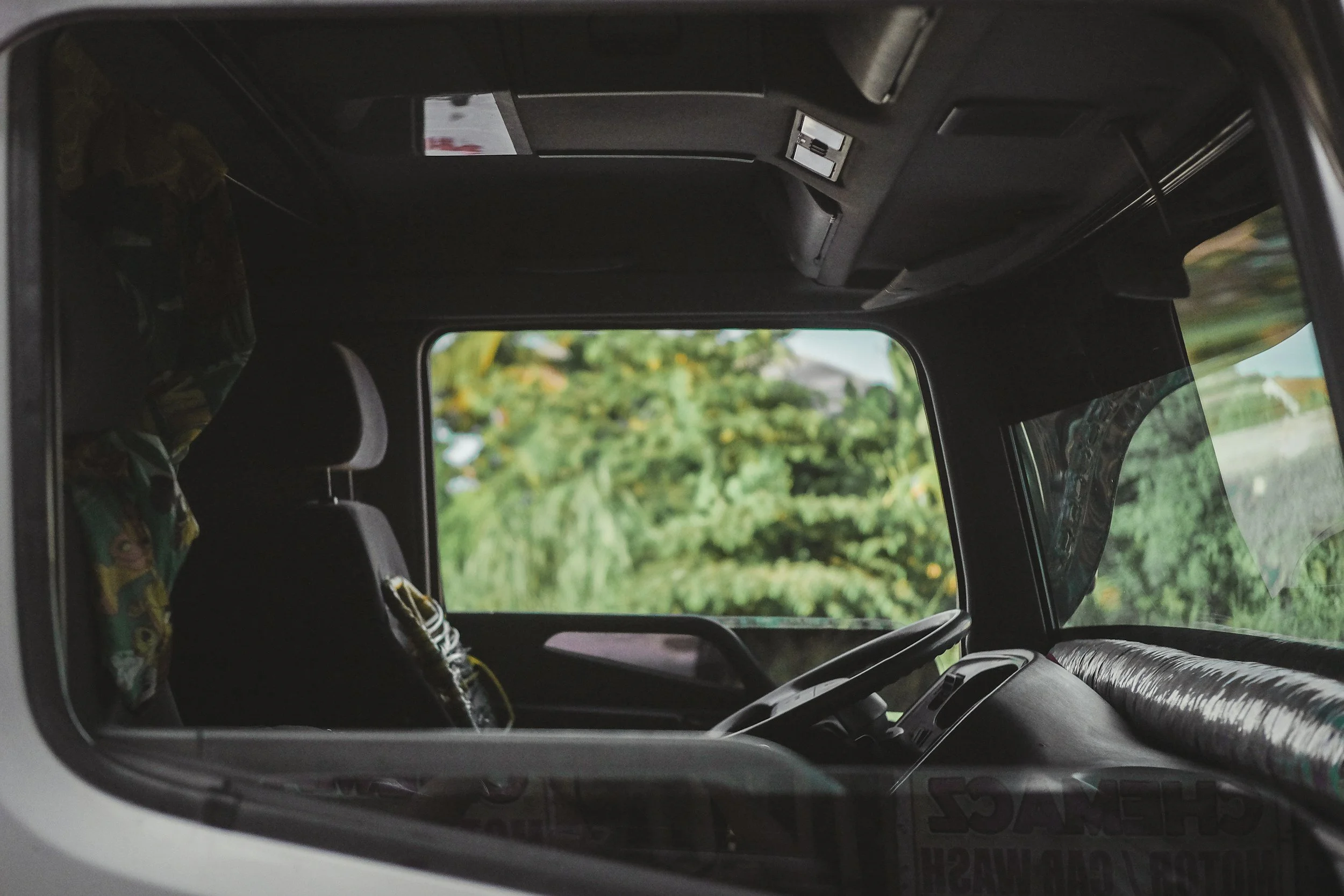 View of the interior of a vehicle through a rear window, showing headrests, a child's seat, and blurred greenery outside.