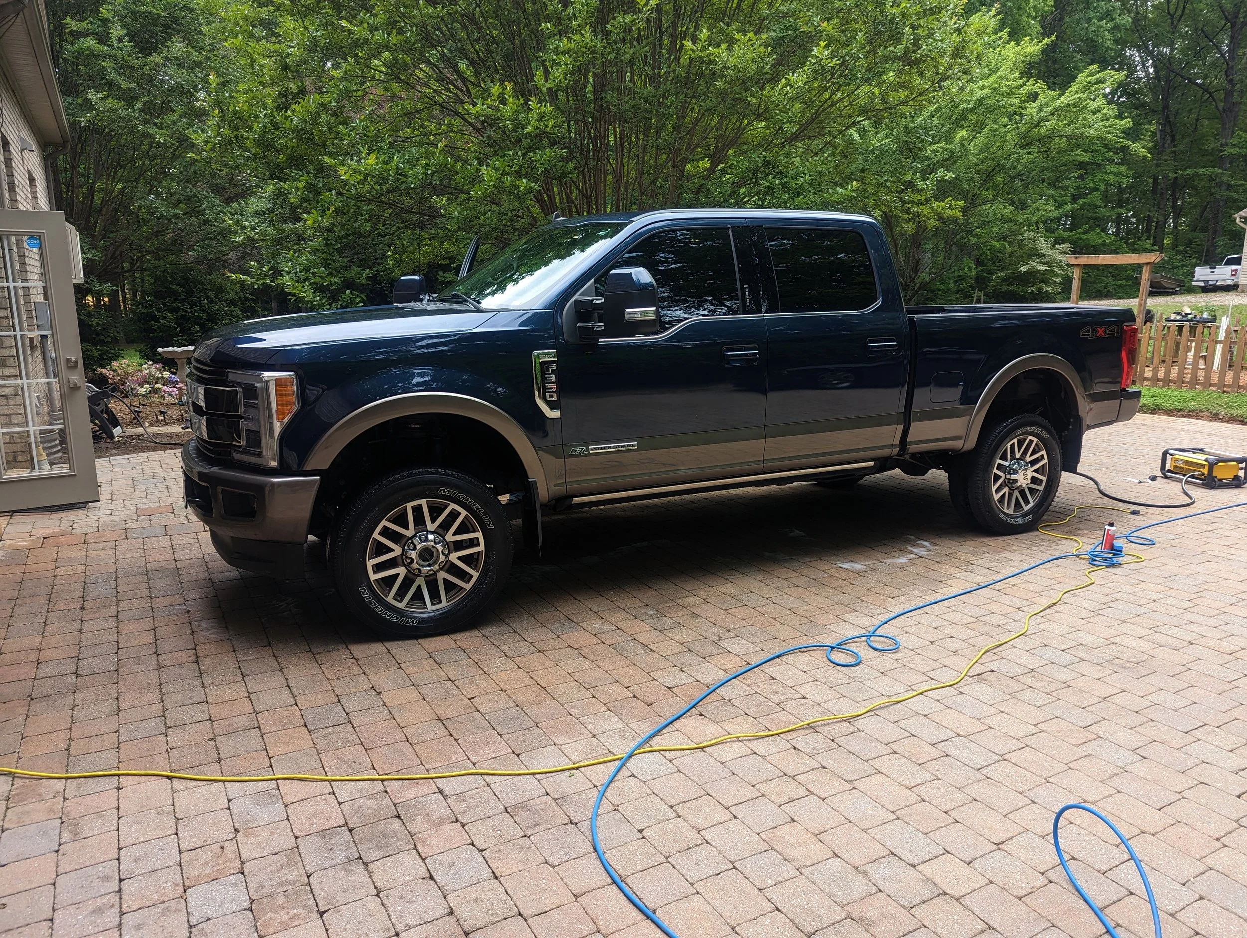 A black Ford pickup truck parked on a brick patio, with trees and a wooden fence in the background.
