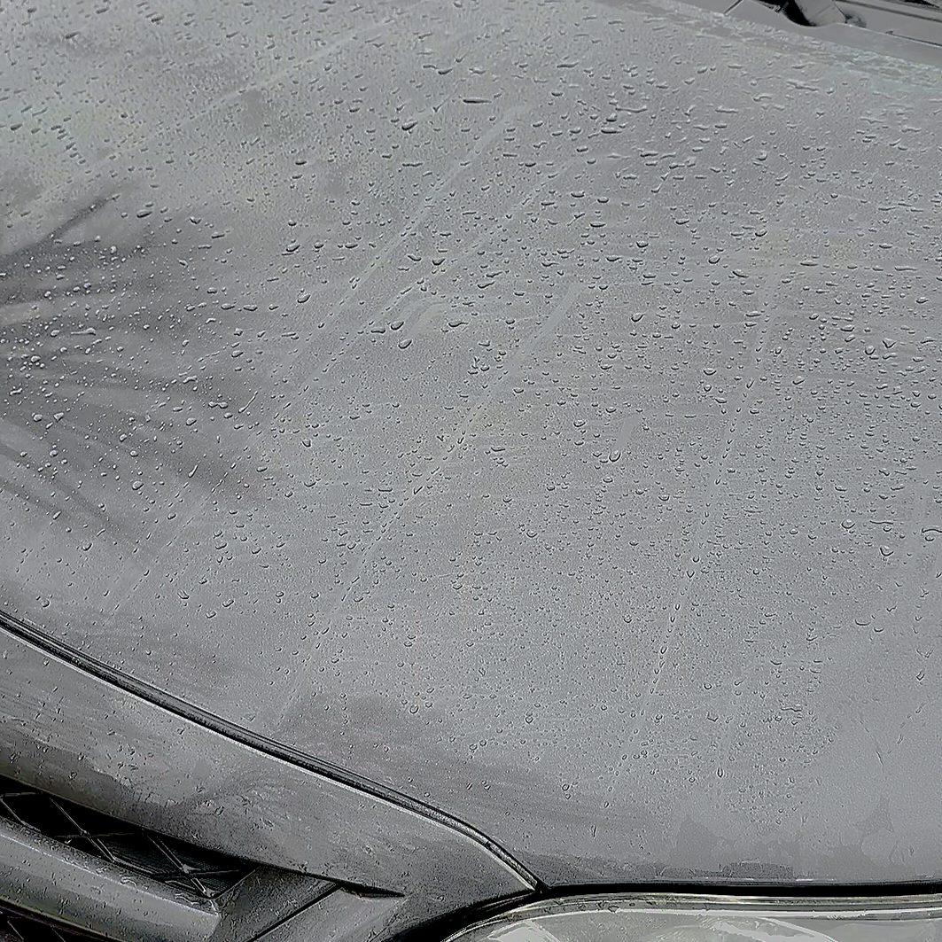 Close-up of a silver car's hood with raindrops on its surface.
