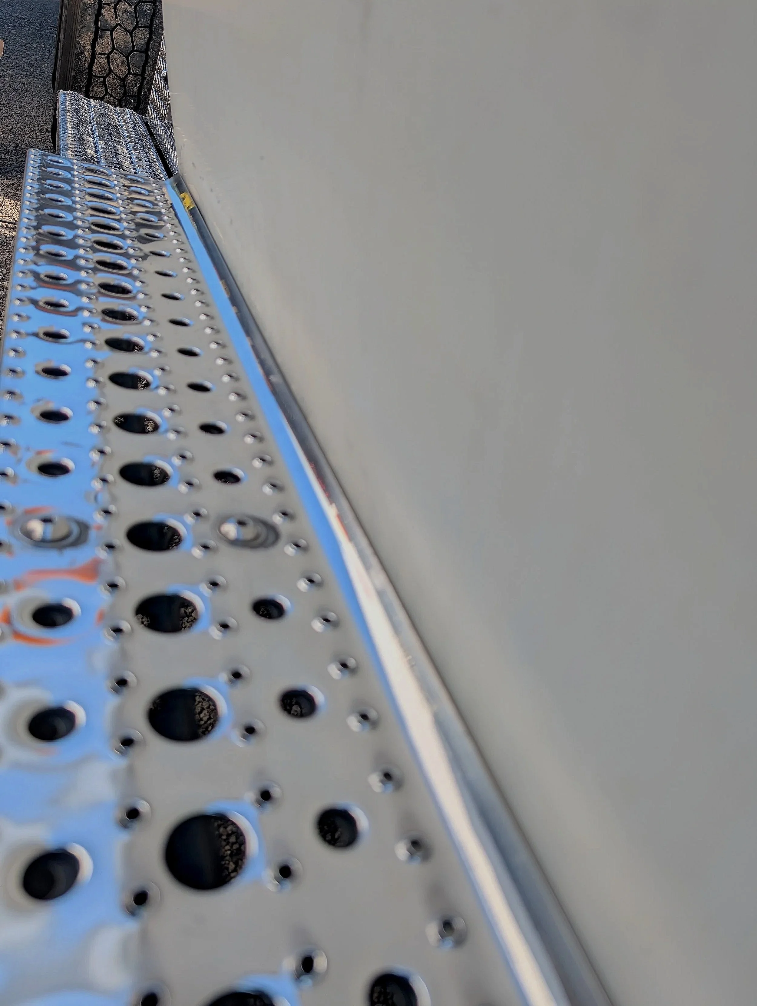 Close-up of a metallic object with multiple circular holes, reflecting light, set against a blurred background.
