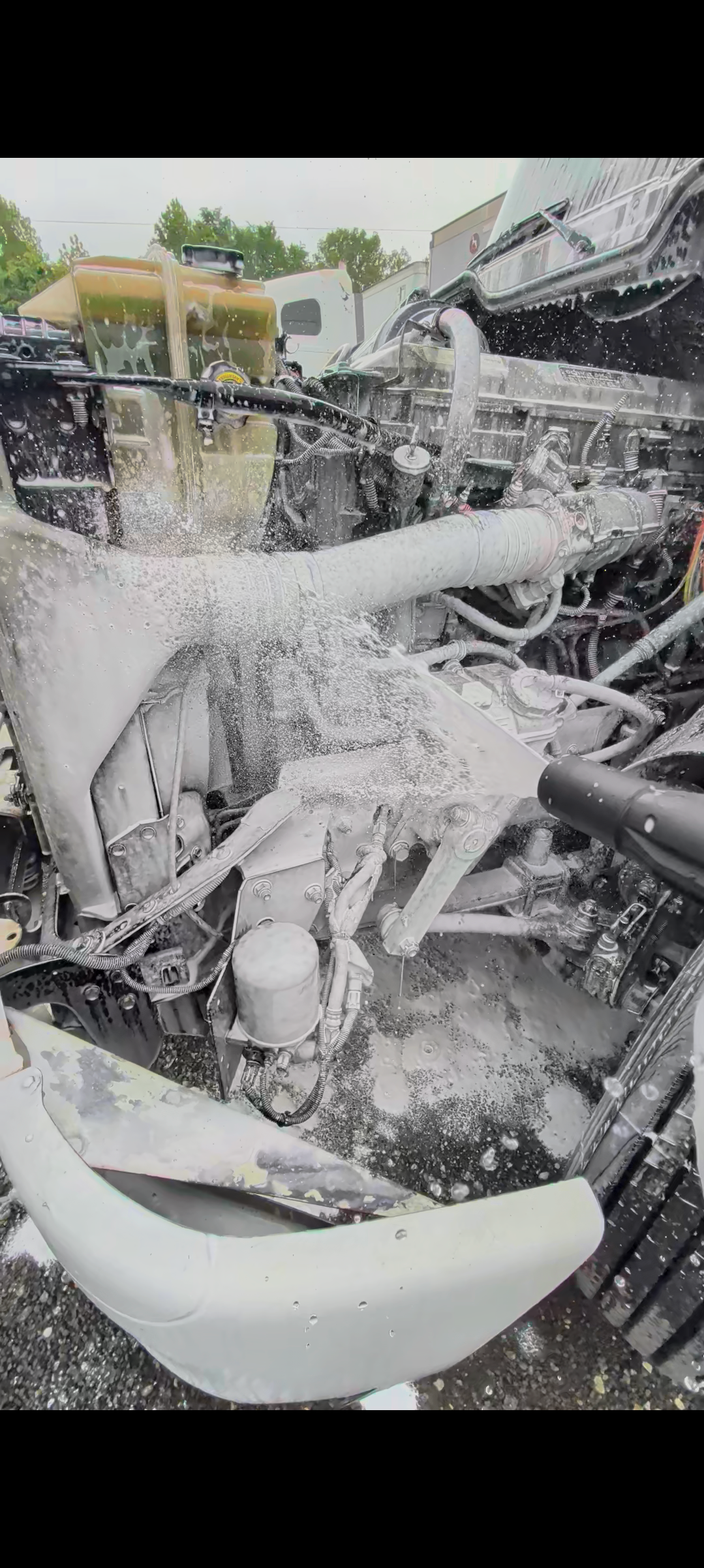 Close-up of a damaged car engine with water spraying, showing various mechanical parts and wires.