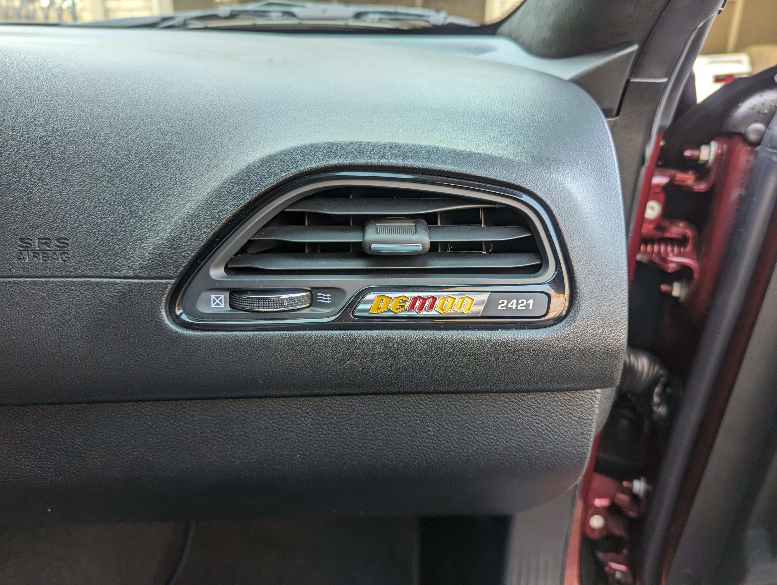 Car interior dashboard with air vent and a badge that reads 'Demon 2421'
