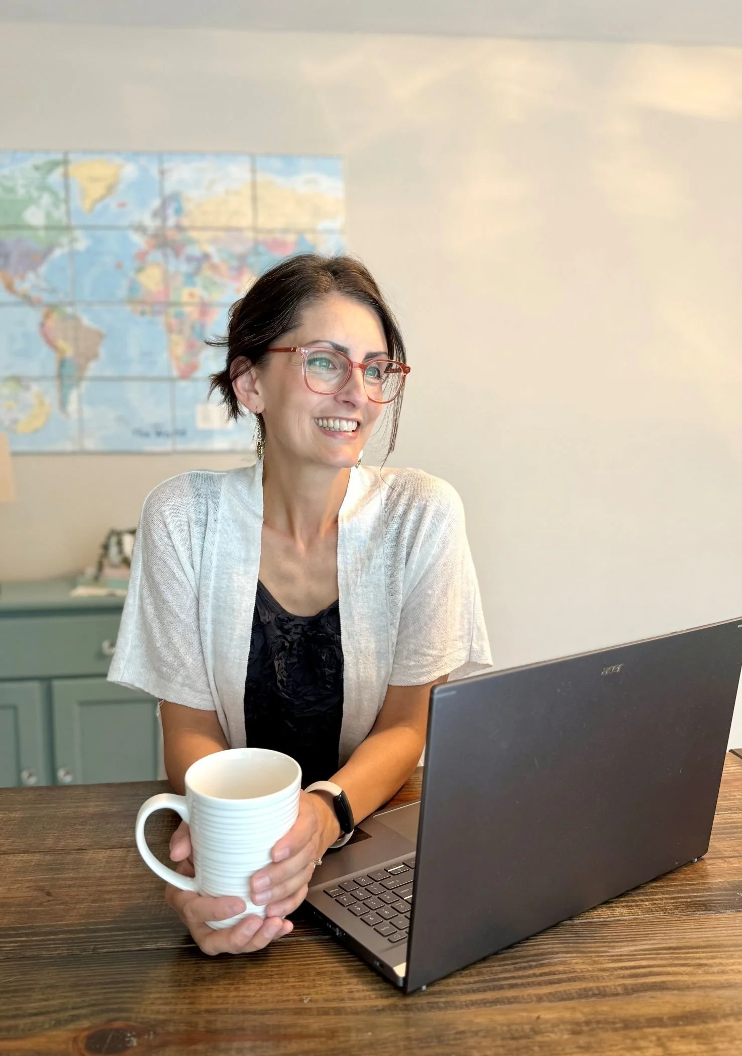 elizabeth daniels smiling with white mug in hand while sitting at wooden table with open laptop