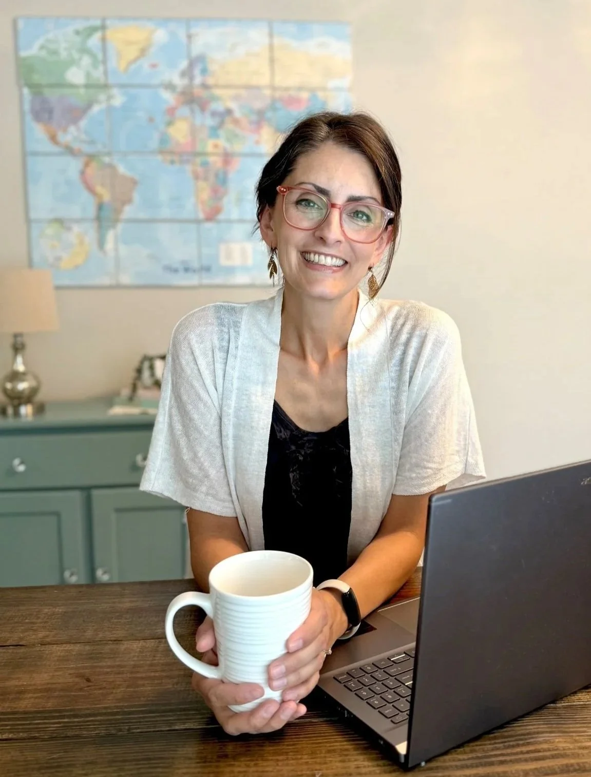 elizabeth daniels wearing pink glasses holding white mug sitting behind laptop smiling