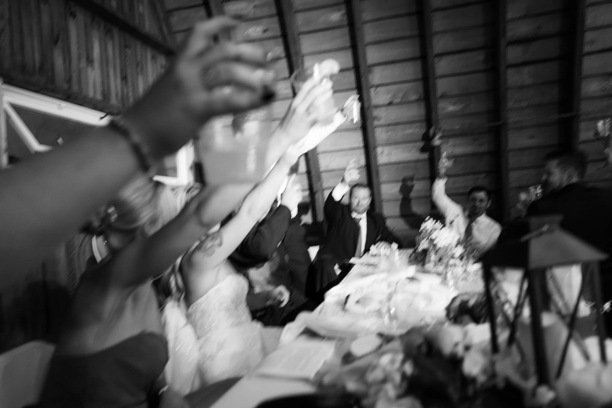 People raising glasses in celebration at a table during a gathering, in a rustic indoor setting with wood-paneled walls.