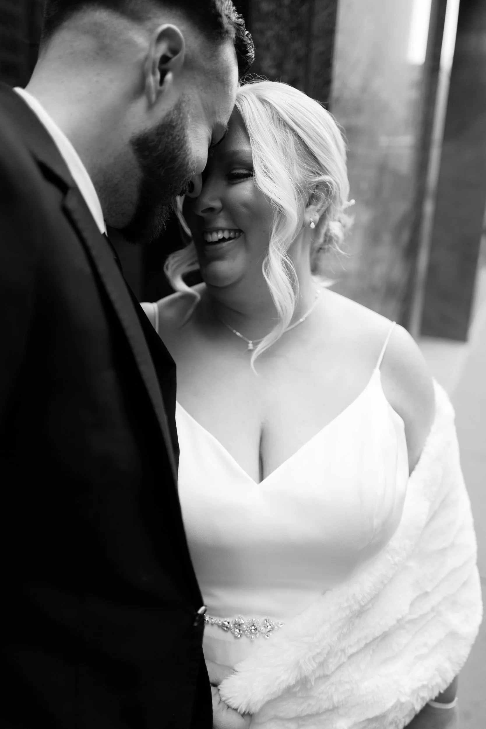 A bride and groom share an intimate moment, touching foreheads and smiling at each other.