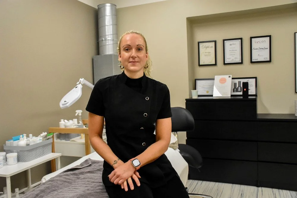 En kvinne i svart arbeidstøy sitter på en behandlingbenk i et klinikk- eller spa-miljø.