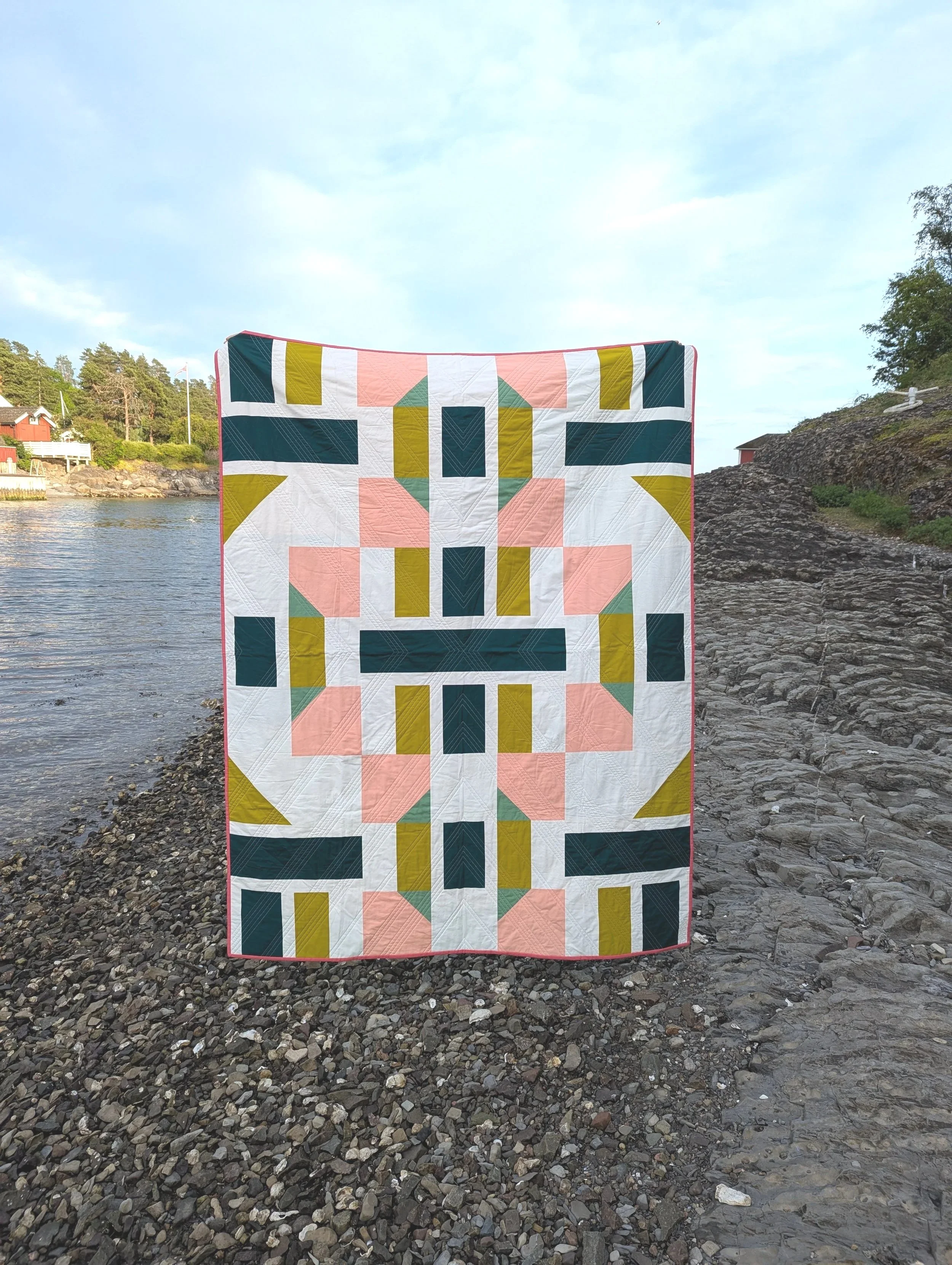 Modern geometric quilt being held on a rocky beach