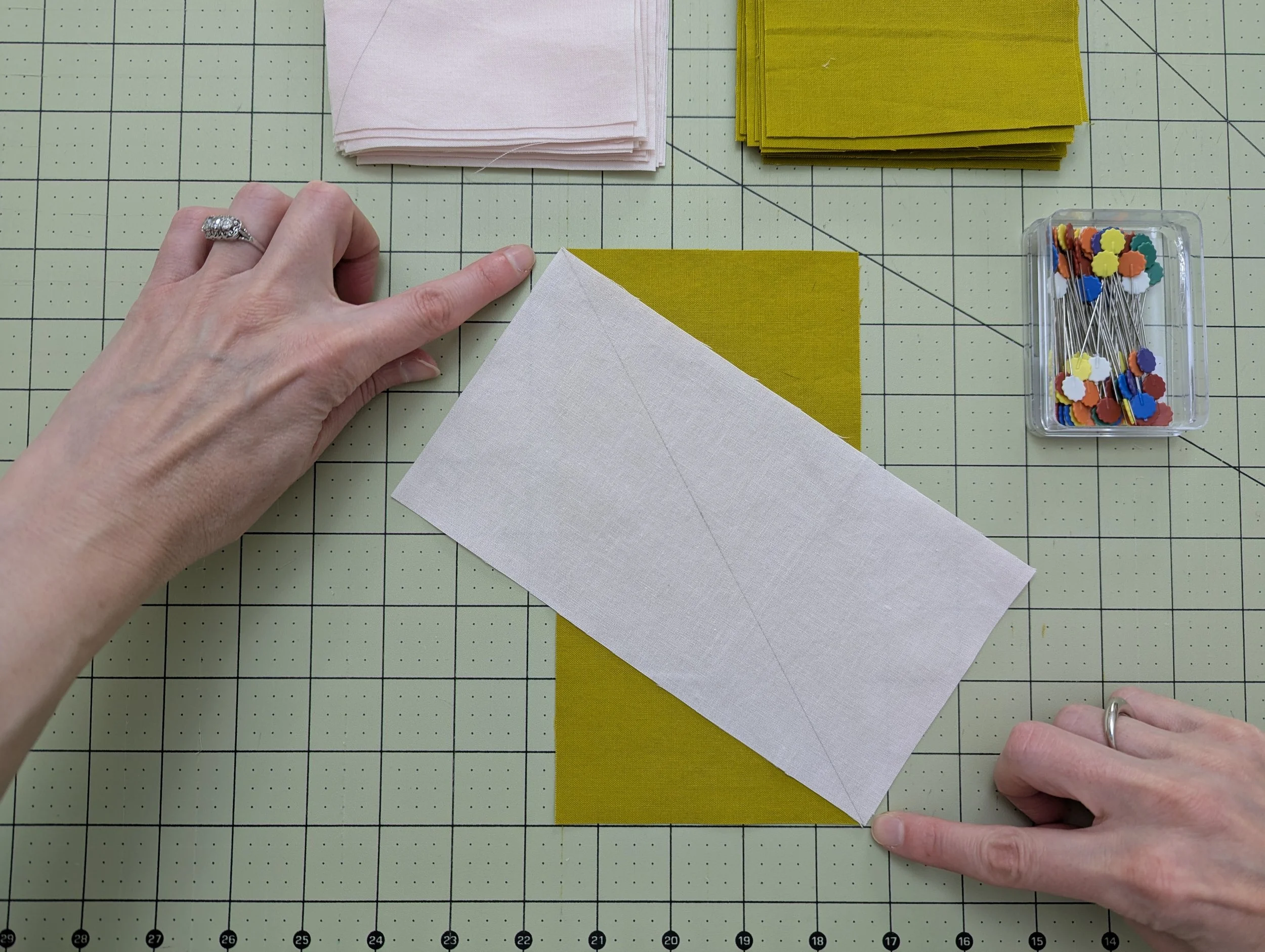 Putting rectangles together to make HRTs, with pink and green pieces of fabric positioned on a cutting mat