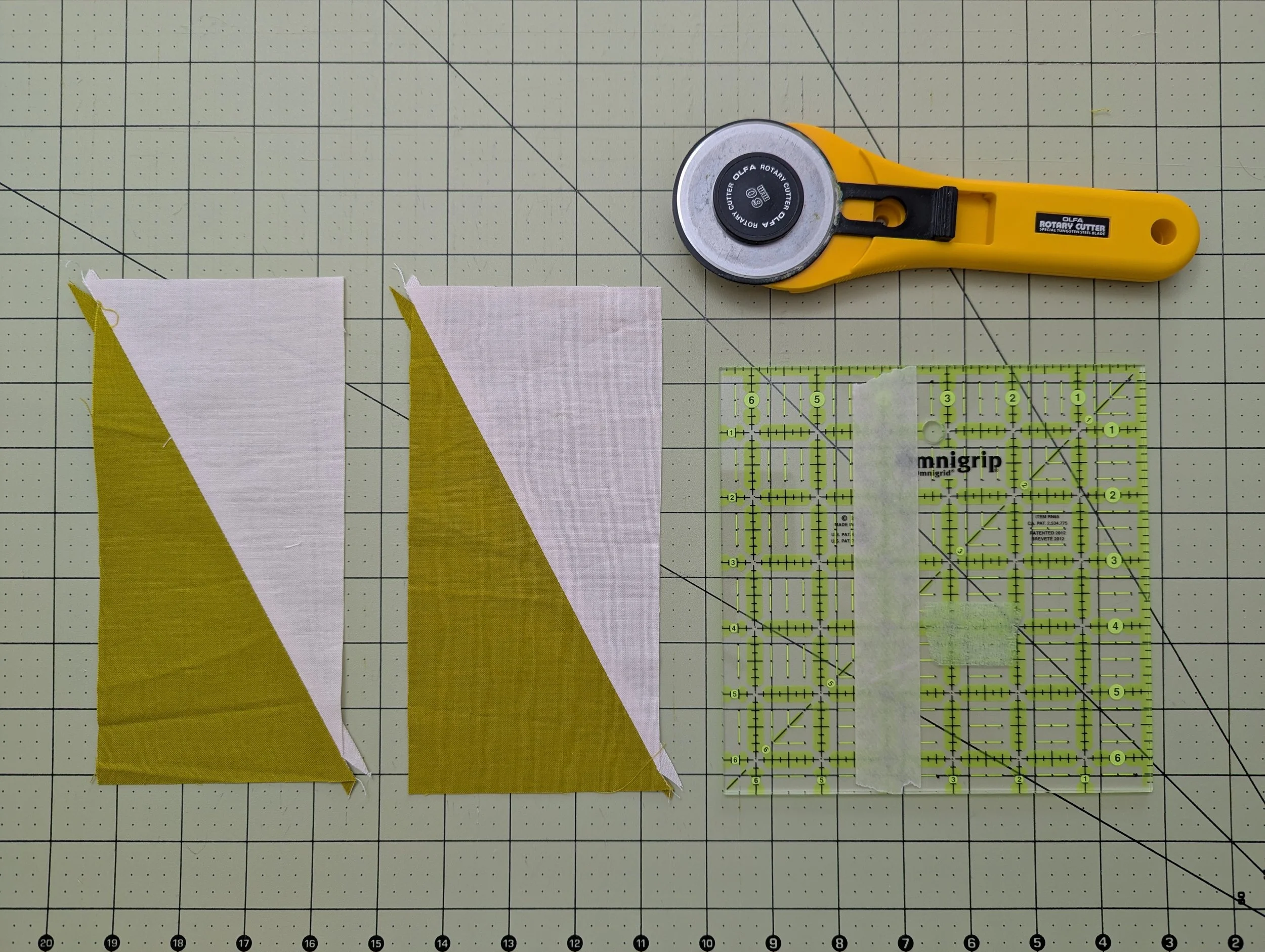 Two pink and green colored HRT blocks with a ruler and a rotary cutter on a cutting mat, ready to be trimmed