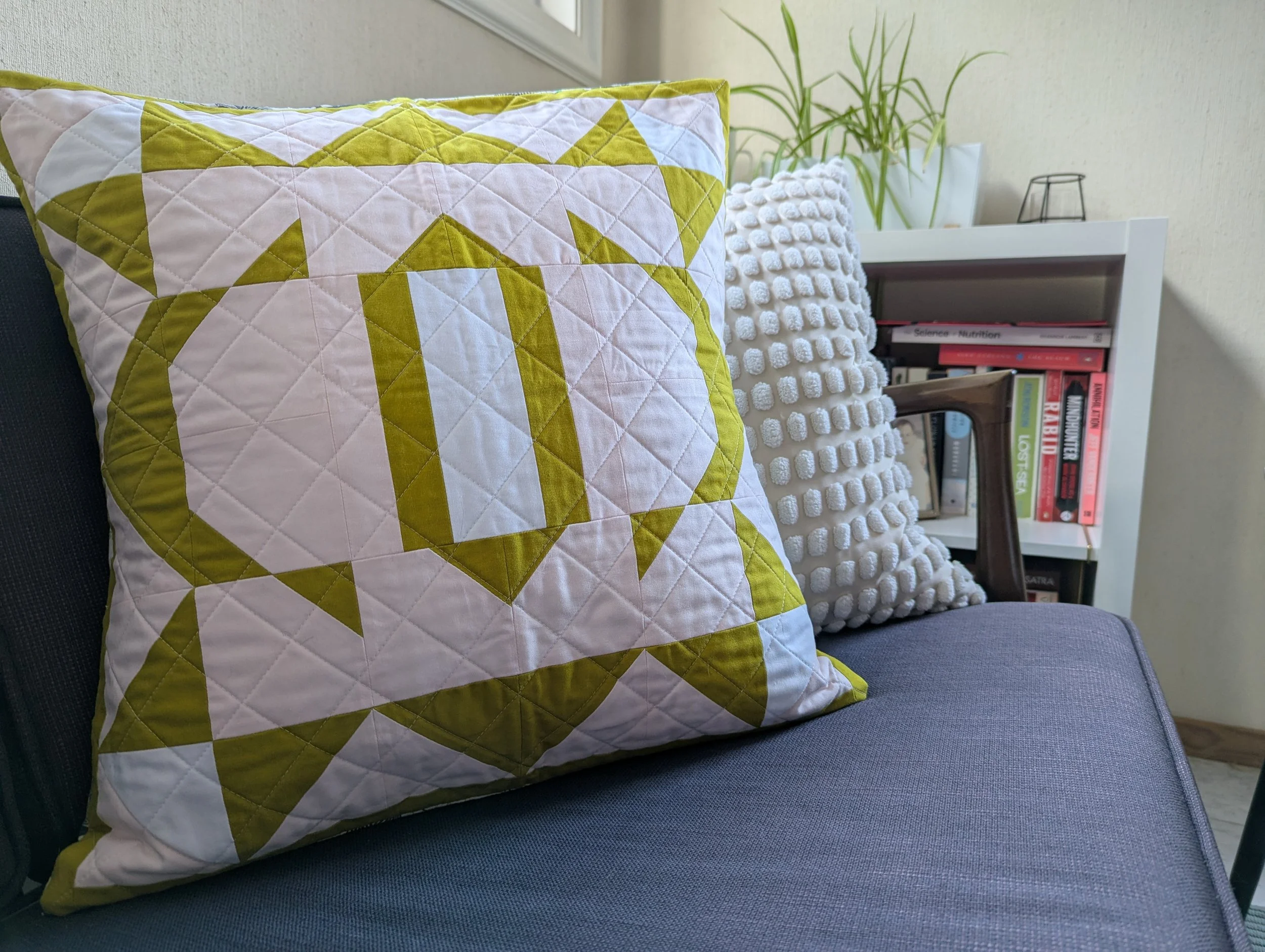 Cushion version of The 2995 Quilt by Millie & Bun Designs- a modern geometric quilt in pink, yellow, and white colors on a blue couch.
