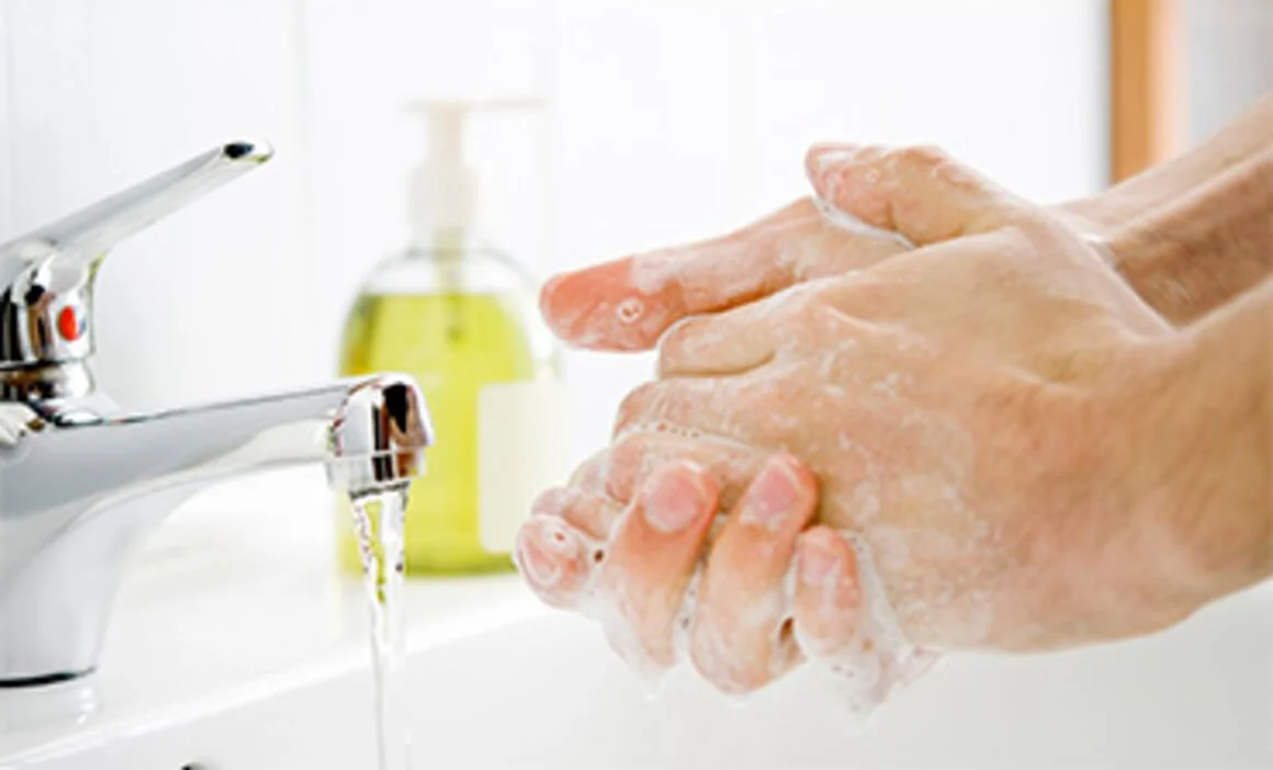 Person washing hands with soap and water at bathroom sink.